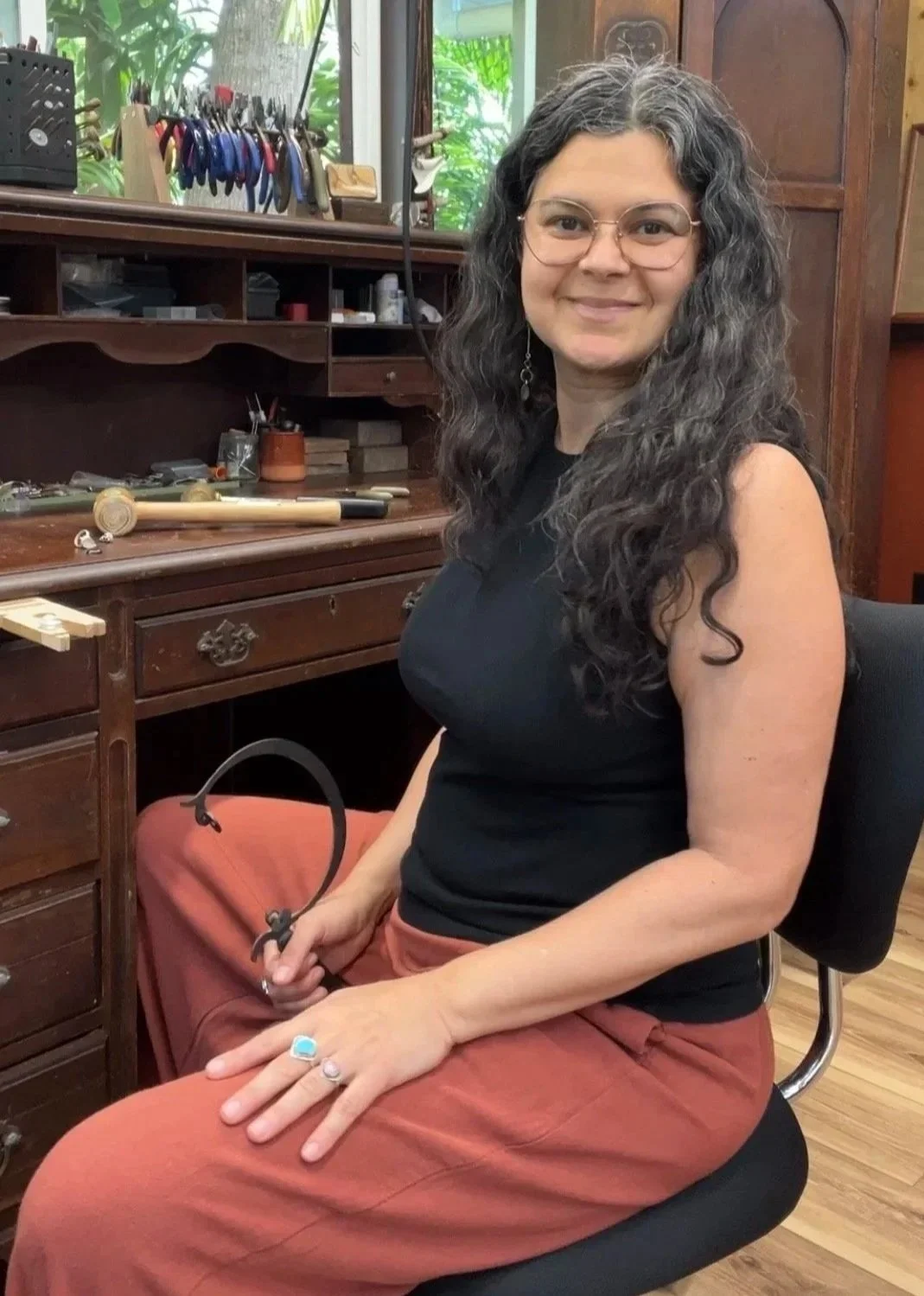 Jewelry instructor seated at a traditional jeweler’s bench in a professional silversmith studio, surrounded by jewelry making tools, demonstrating techniques used in jewelry making classes and workshops on the Big island of Hawaii near Hilo.