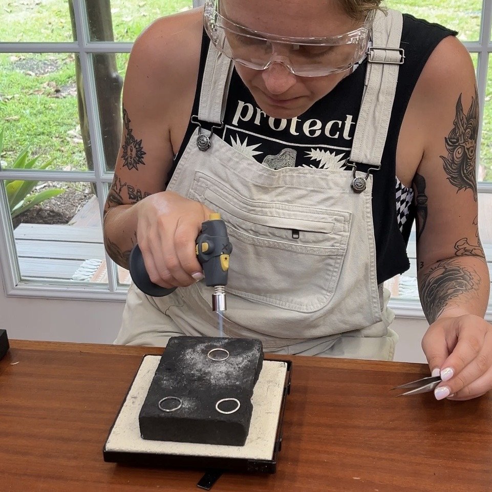 Student soldering sterling silver stacking rings with a jewelry torch in a silversmithing class.