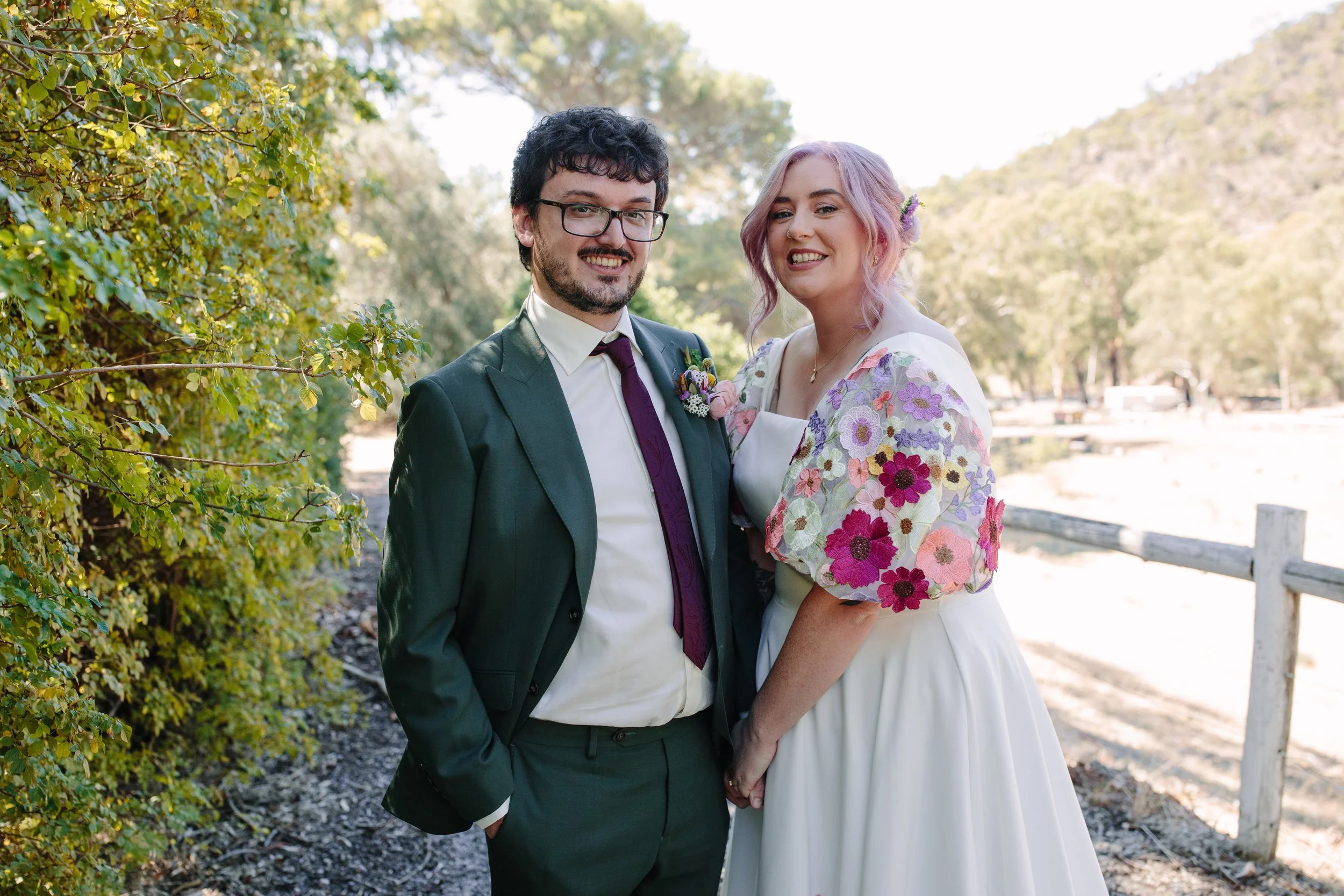 Bride and groom holding hands during portraits at Marybank Estate in the Adelaide Hills, with colourful floral wedding attire and picturesque countryside surroundings.