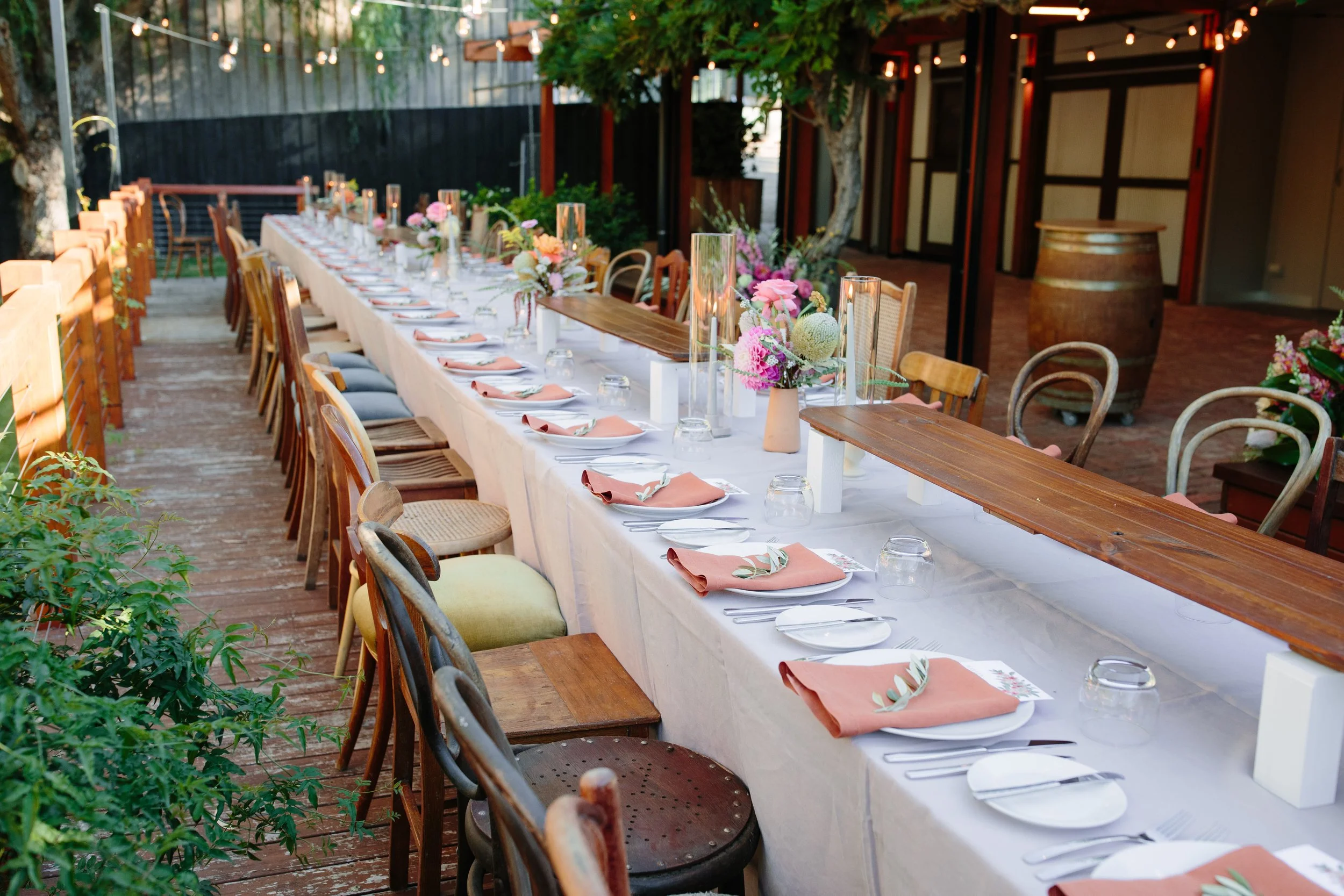 Single long reception table styled with colourful florals and candlelight beneath wisteria-covered trees at Marybank Estate, creating an intimate wedding dinner for 50 guests.