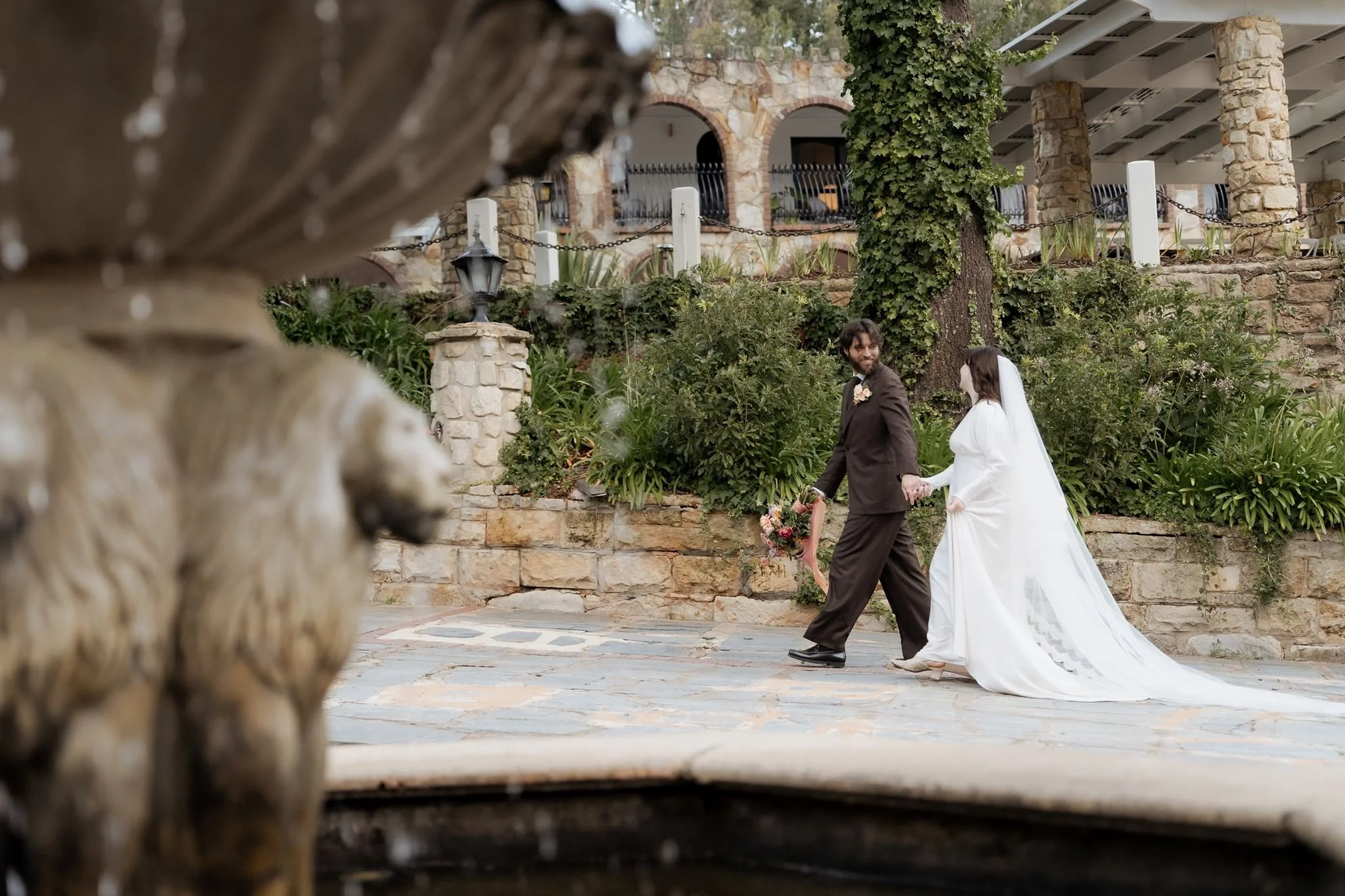 Couple walking hand-in-hand by the fountain at The Manor Basket Range during their romantic Adelaide Hills wedding.
