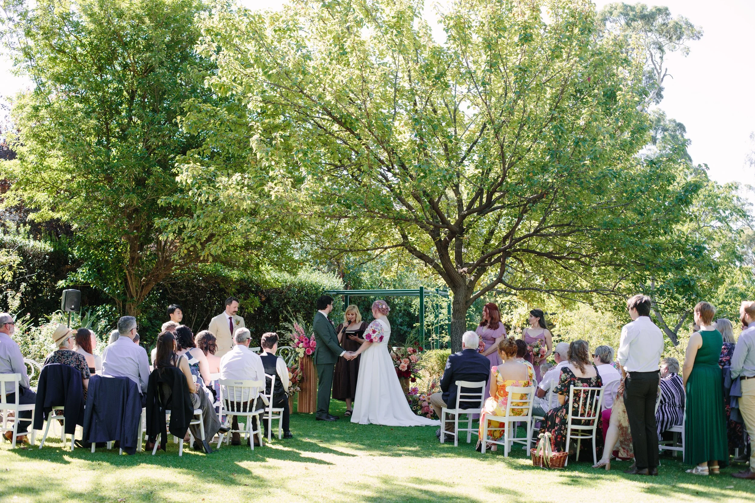 Bride and groom standing beneath a large tree during their outdoor wedding ceremony at Marybank Estate in Adelaide, surrounded by 50 guests and warm autumn florals.