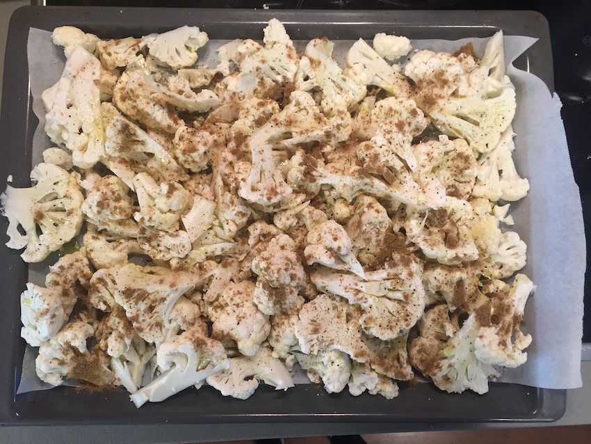 Cut up cauliflower with olive oil and cumin, ready for the oven. 