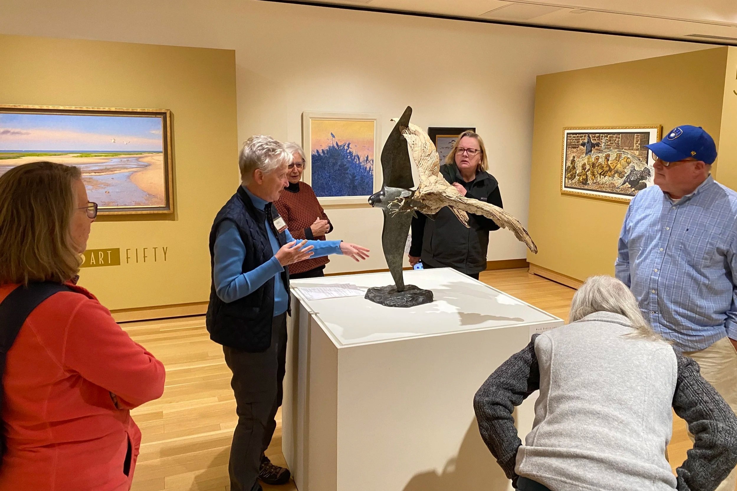 A museum docent discusses a peregrine falcon sculpture that is part of the Birds in Art exhibit at the Leigh Yawkey Woodson Art Museum to SoWBA members visiting.
