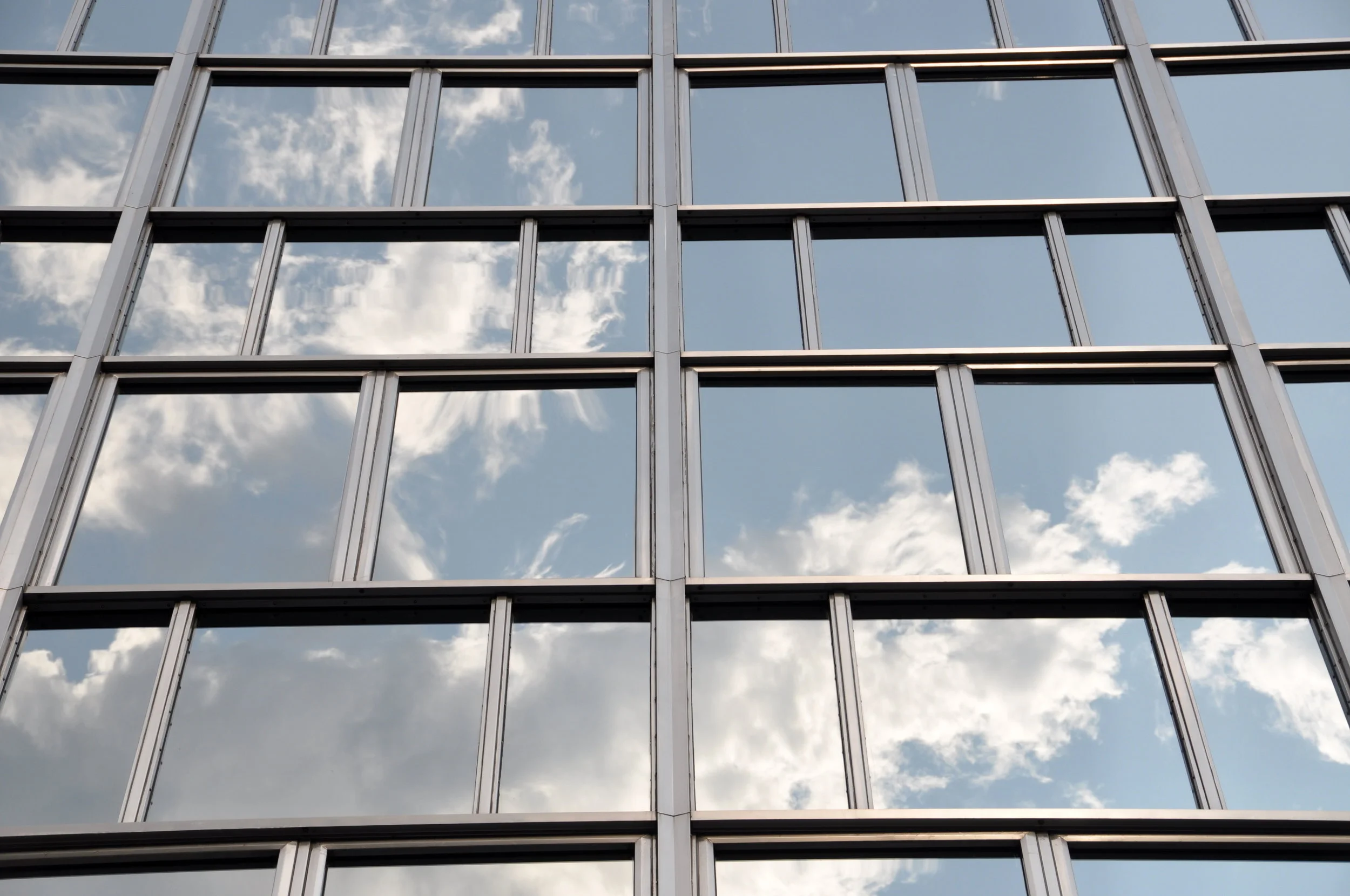 A glass-fronted building reflects clear sky. Photo by Kevin Harber