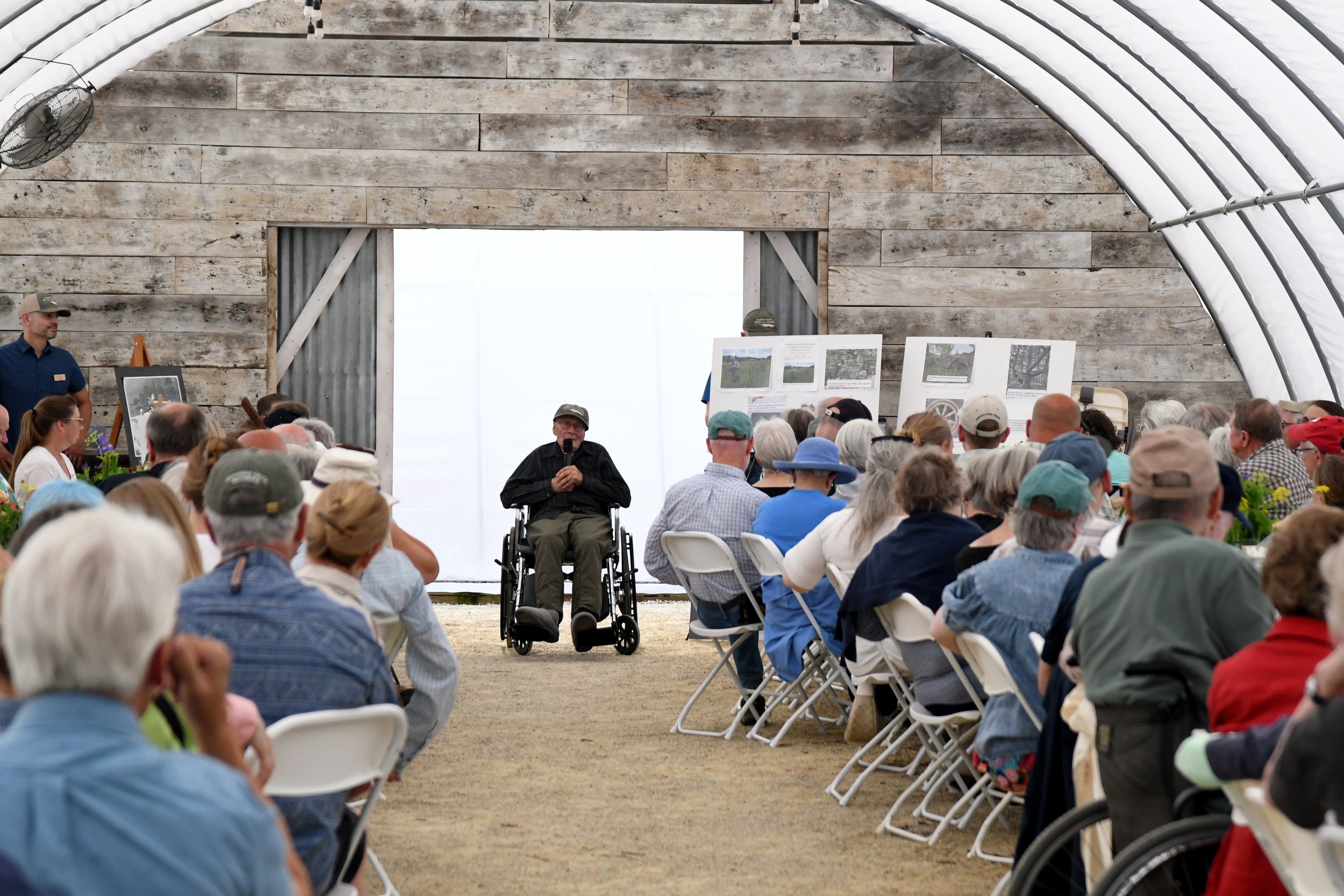 David Gunnulson holds a microphone at the front of the room and tells stories to those gathered in the Sprouting Acres hoophouse