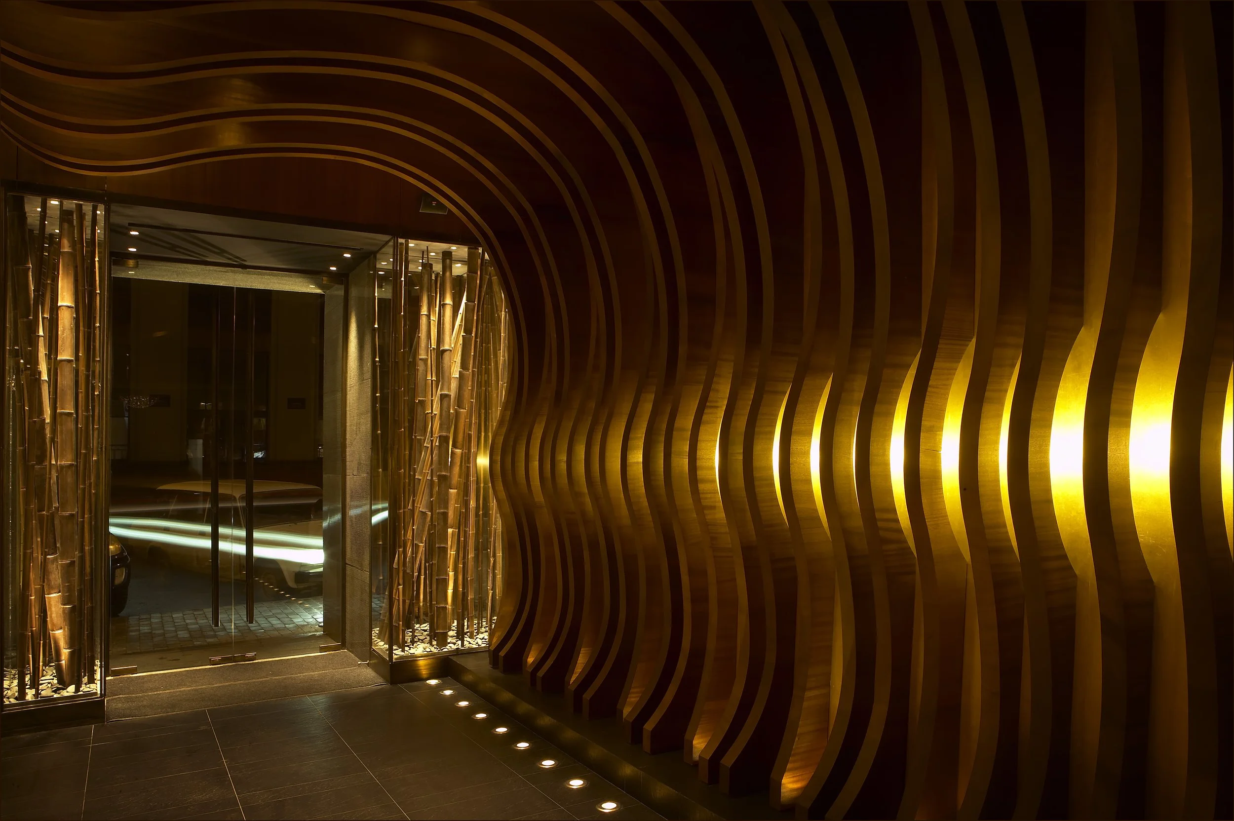 Sculptural entrance to Nobu Moscow featuring illuminated curved walnut MDF ribs and an immersive hospitality design.