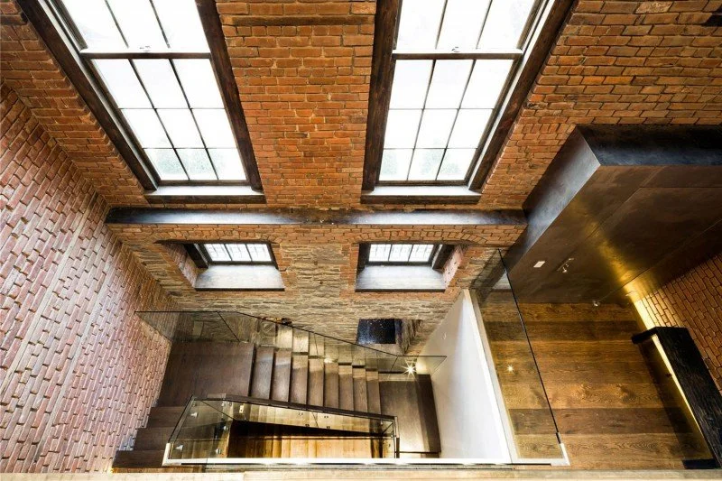 Staircase at 80 Washington Place in New York, with exposed brick walls, tall windows and a glass railing.