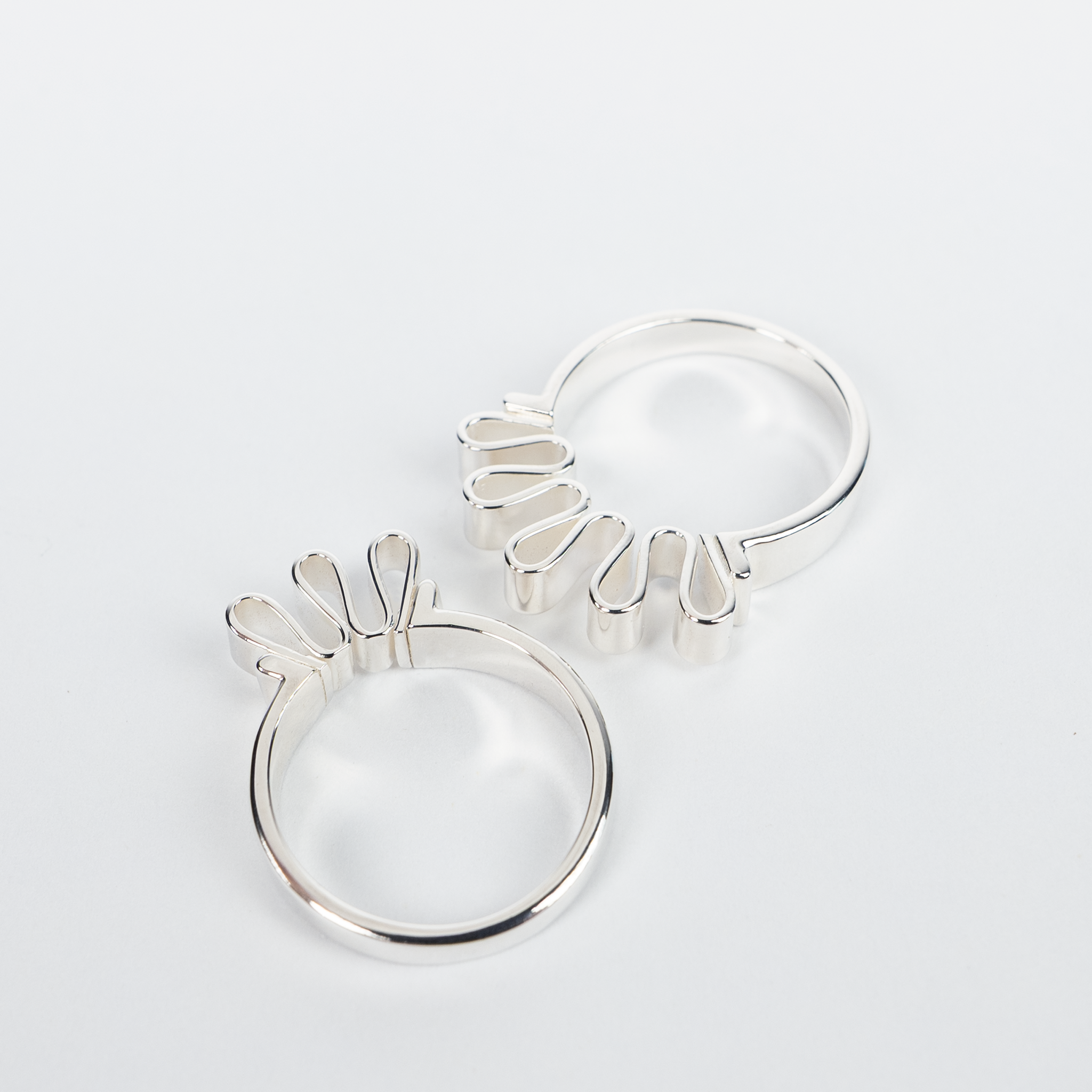 Two silver Ribbon rings with folded sculptural detailing arranged on white background