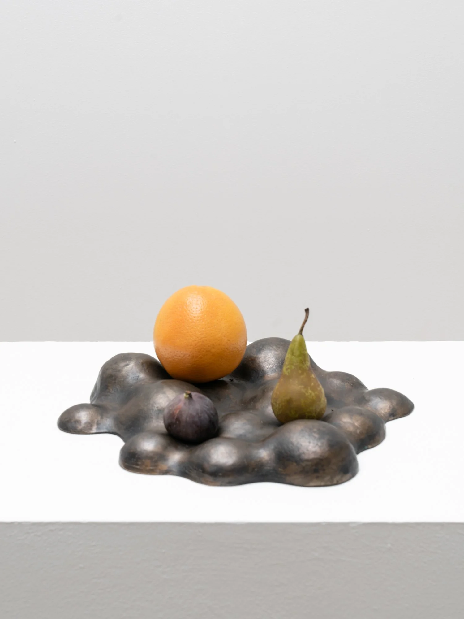 Bronze fruit bowl styled with orange, pear, and fig showing functional sculptural form