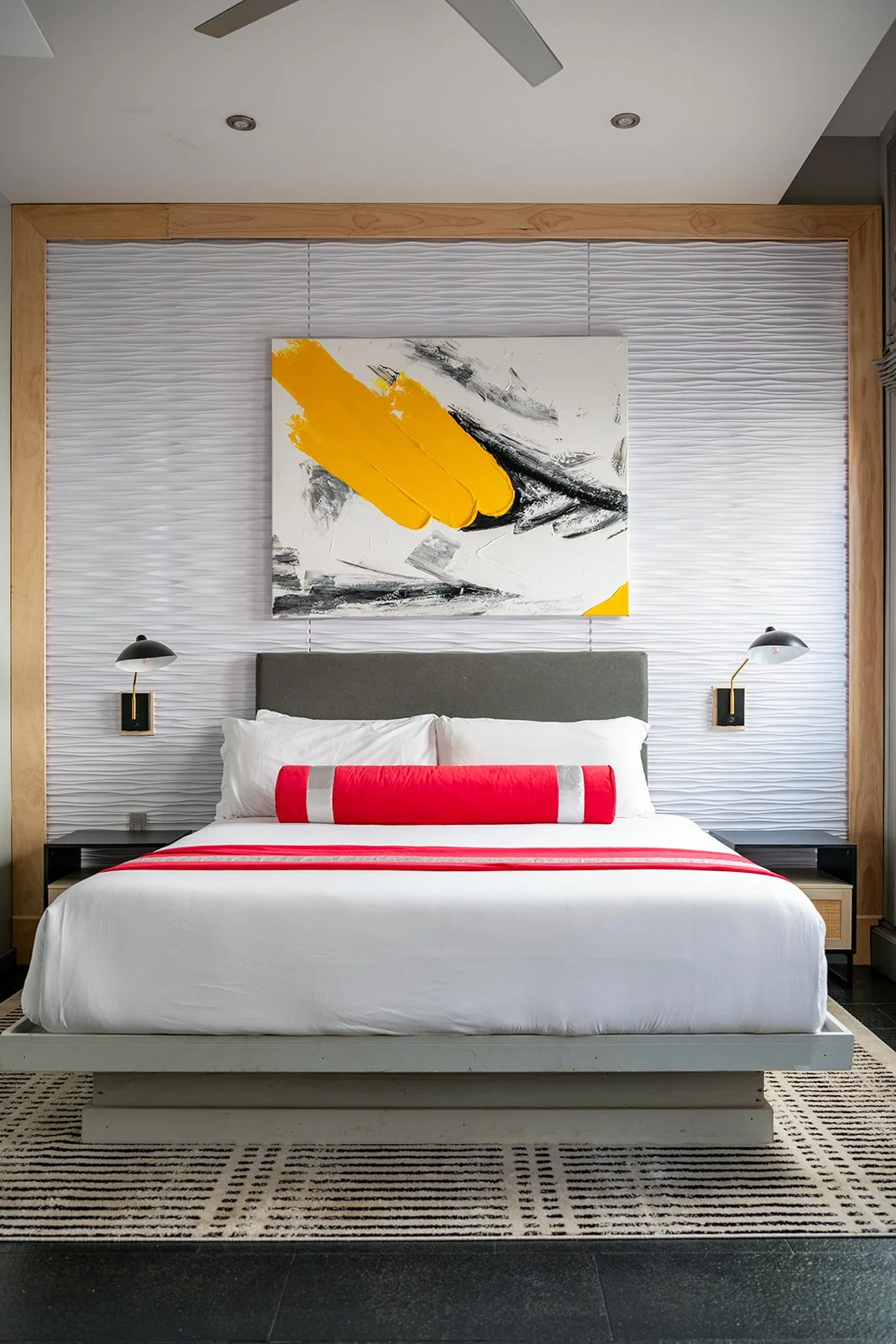 Modern open-concept living room and kitchen with brick accent wall, black leather sofa, abstract artwork, dining table with black chairs, and staircase.