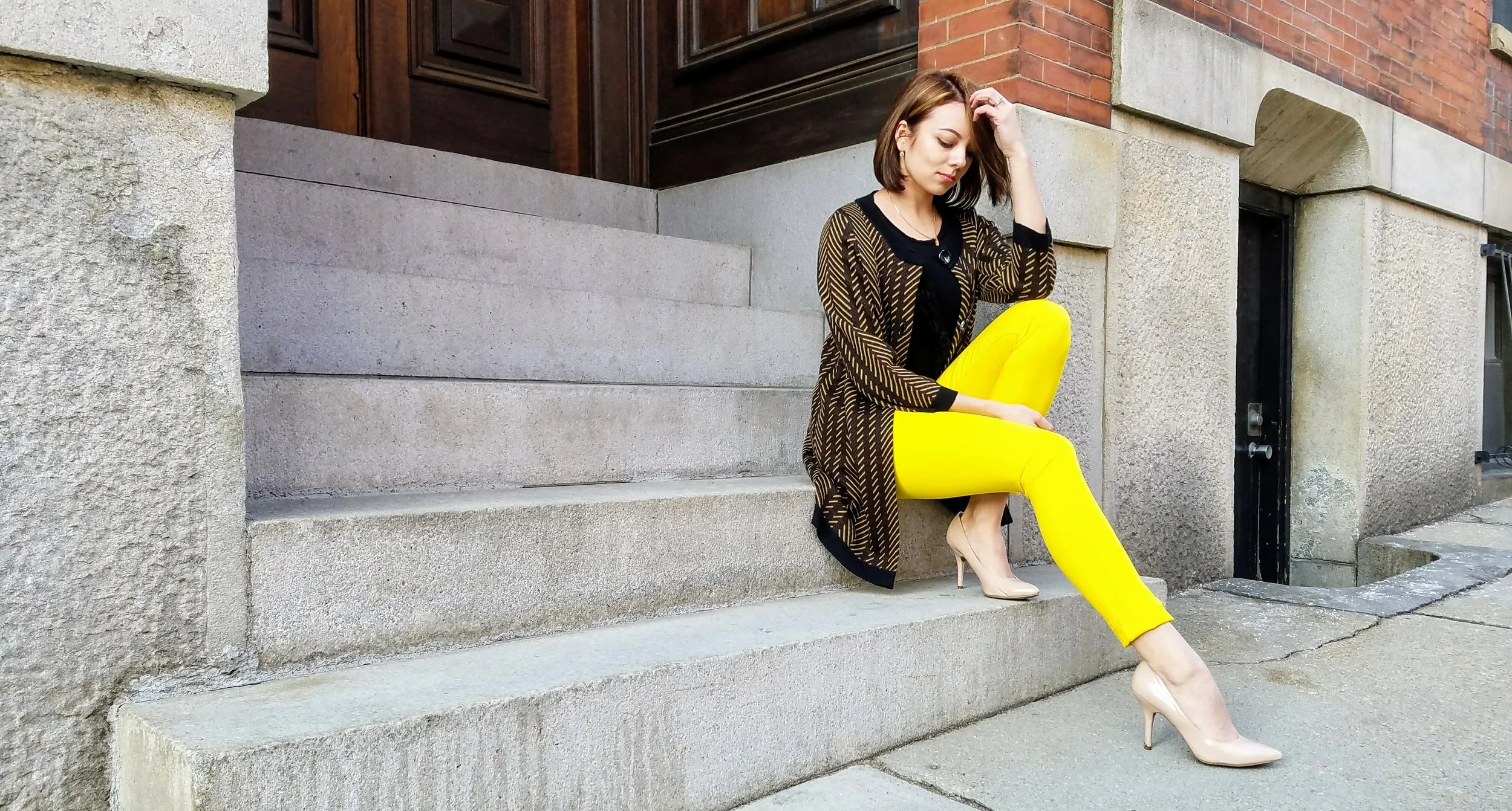 A girl in yellow pants outfit sitting on steps for her blog.
