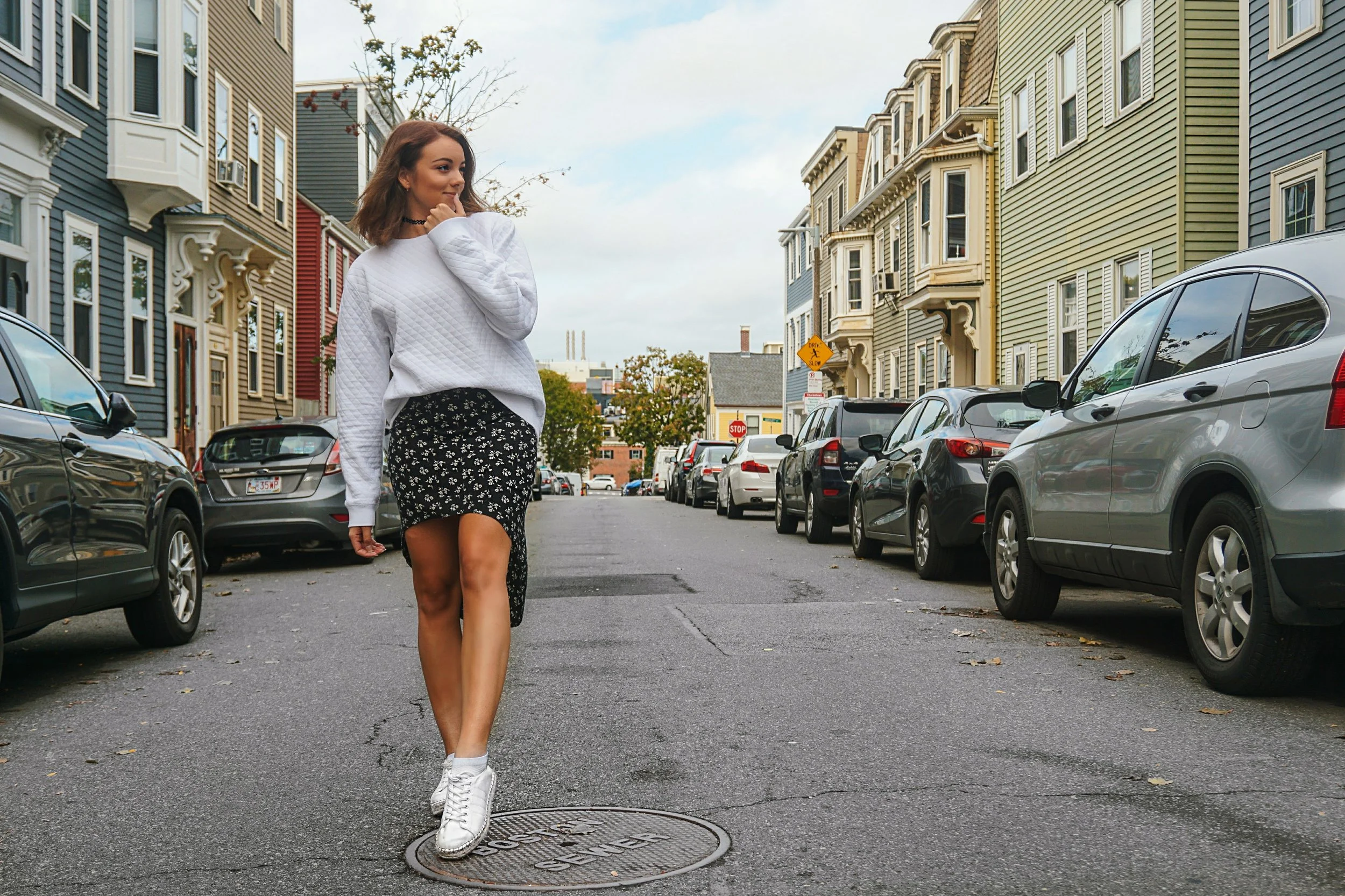 A Boston blogger wearing an oversized white sweatshirt, black skirt, and white sneakers.