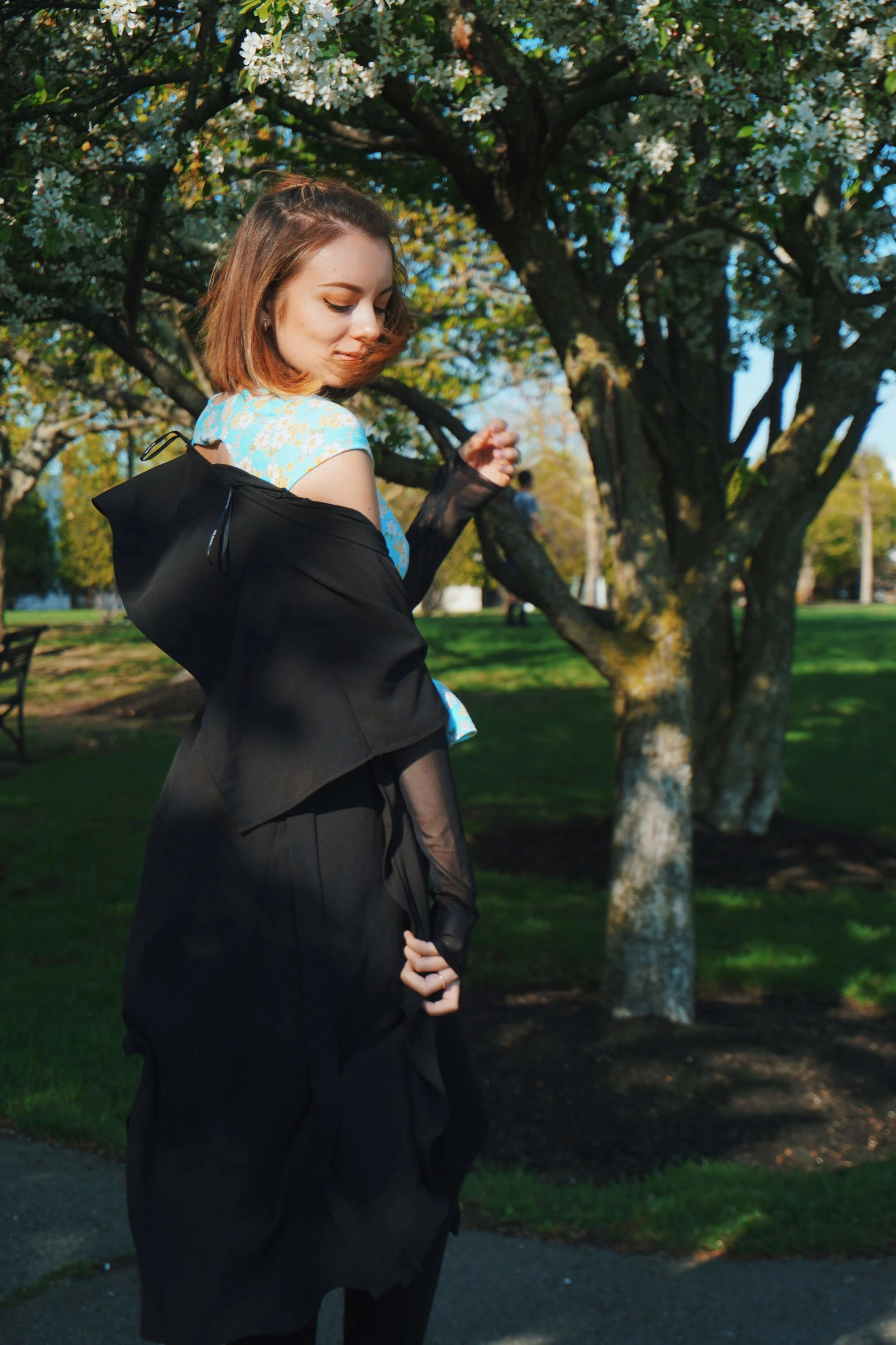 A blogger looking down in the photo, wearing a black duster, blue top, and black capris. 