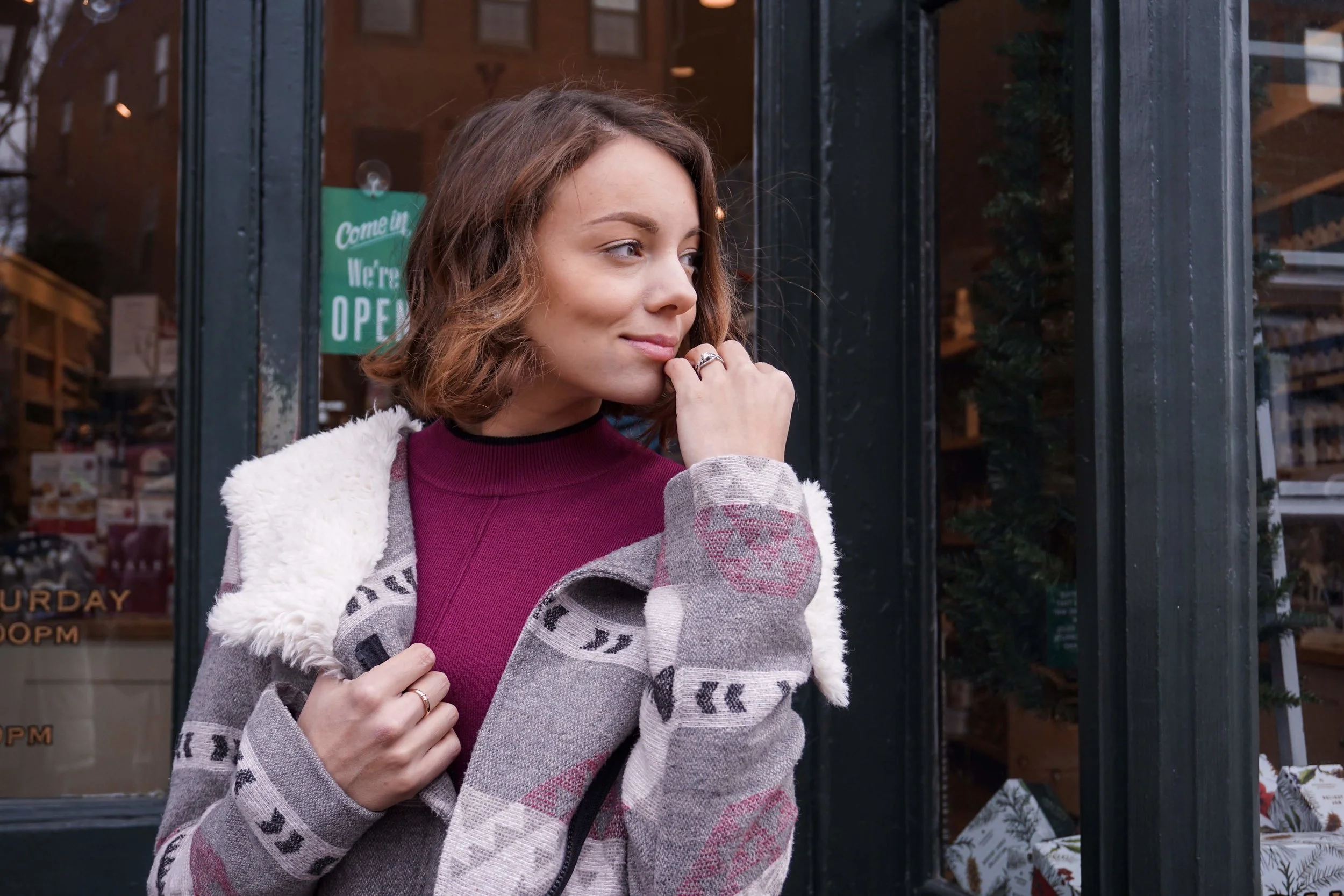 A blogger posing on the street wearing a maroon dress, cozy coat, knee-high boots.