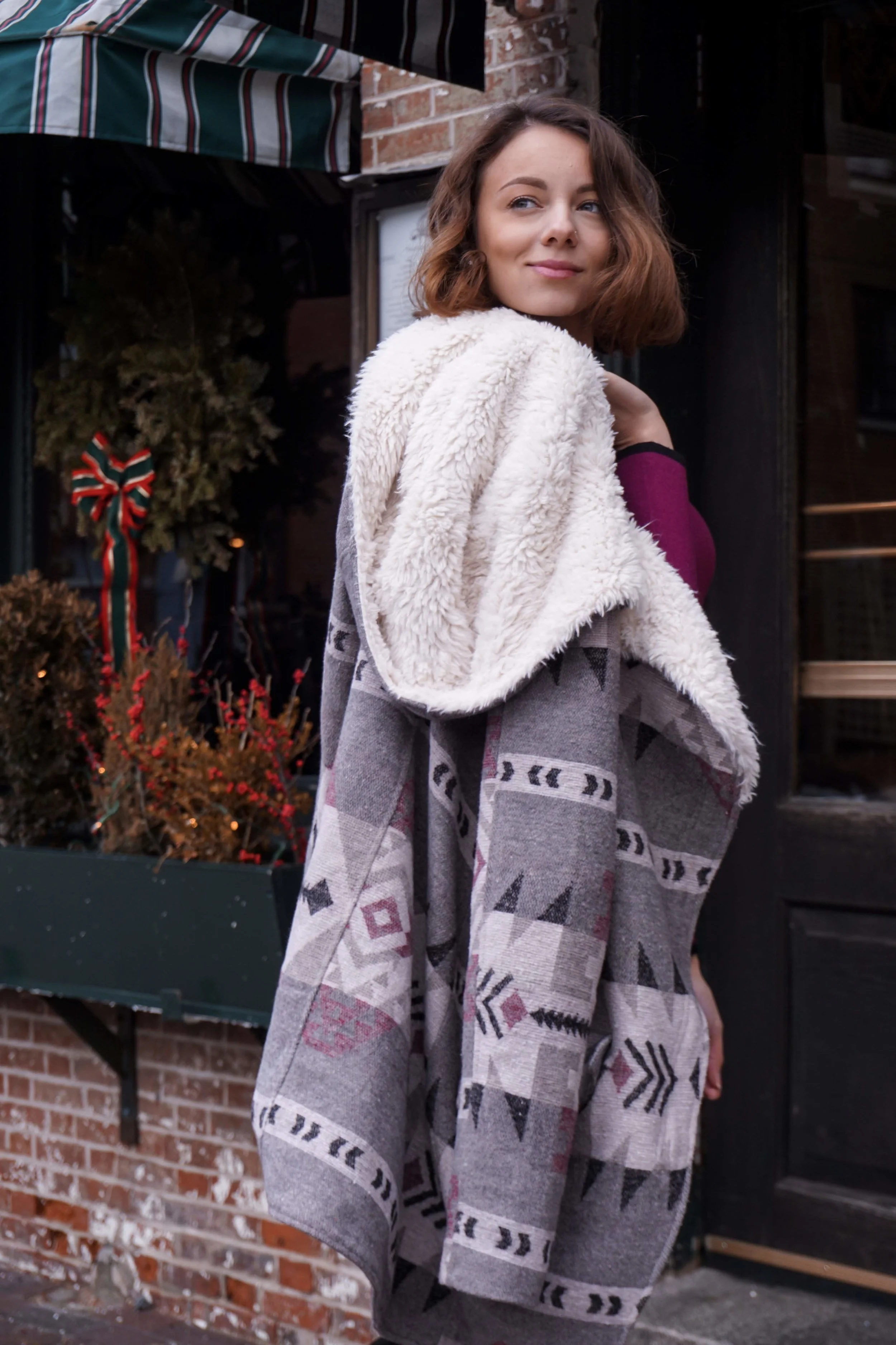 A blogger posing on the street wearing a maroon dress, cozy coat, knee-high boots.
