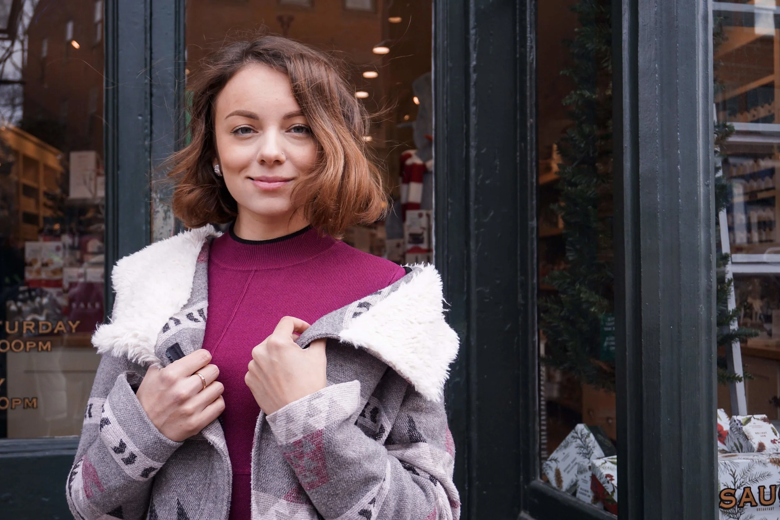 A blogger posing on the street wearing a maroon dress, cozy coat, knee-high boots.