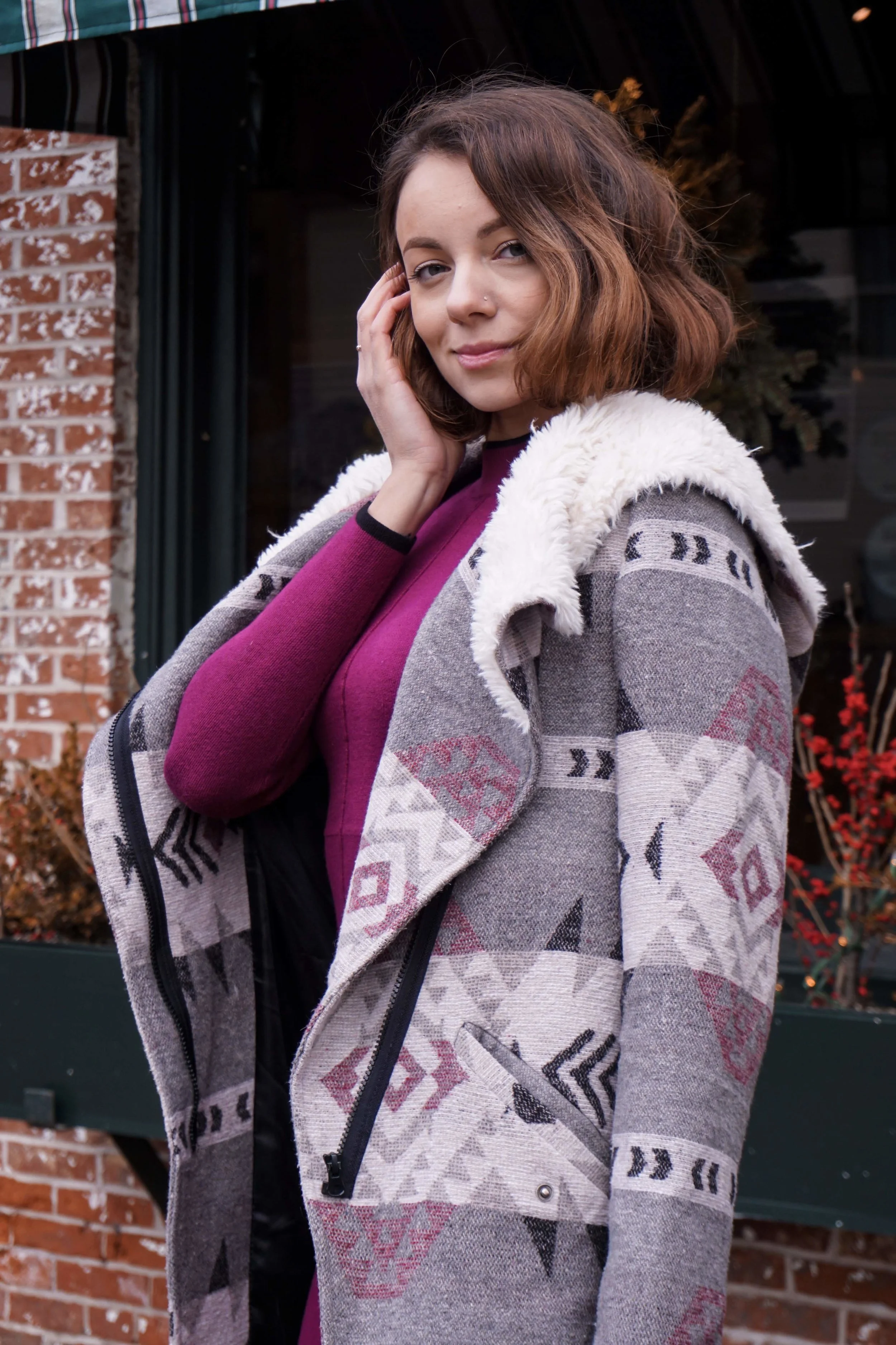 A blogger posing on the street wearing a maroon dress, cozy coat, knee-high boots.