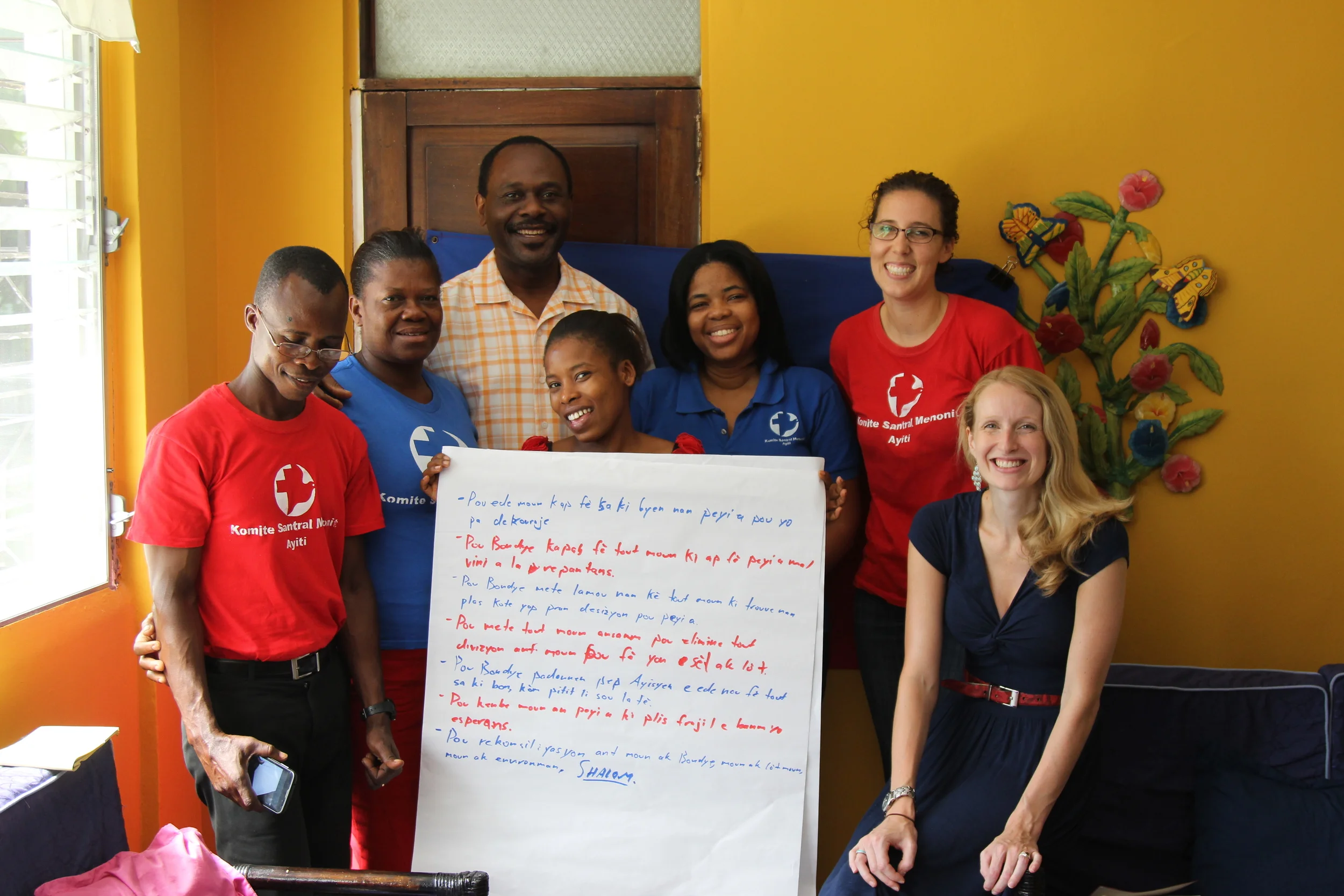 MCC Haiti Port-au-Prince staff: (from left) Joseph, Eclane, Fania (center), Muriel, Katharine, Rebecca with MCC consultant Jose (in back) hold our prayer for Haiti derived from a portion of the Lord's prayer