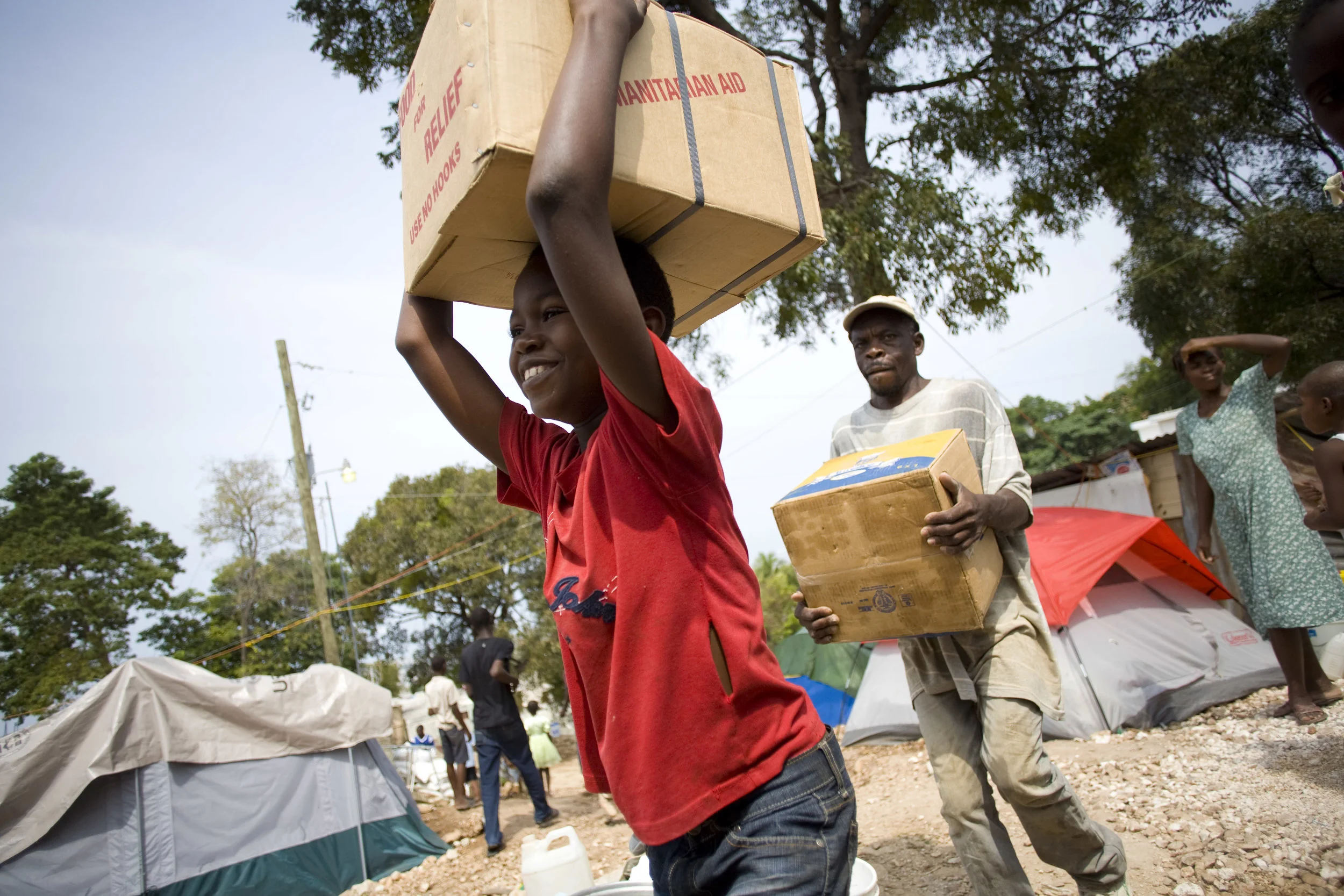 For immediate response, MCC provided canned meat and material aid to local communities. Nicholas Mardoche, pictured above, carries a case of canned meat from a delivery truck to a storehouse in the camp where he lived.