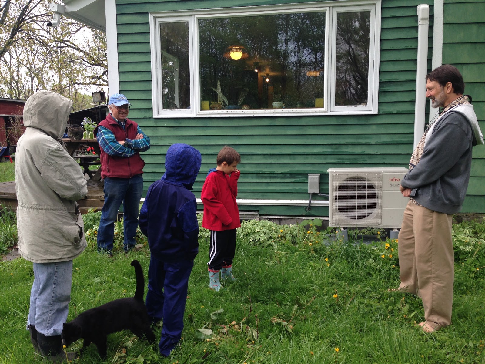 Tom showing the heat pump's compressor unit to a family visiting during a Heat Smart tour; Heat Smart Tompkins coordinator Jonathan Comstock is on right. Photo: Karim Beers
