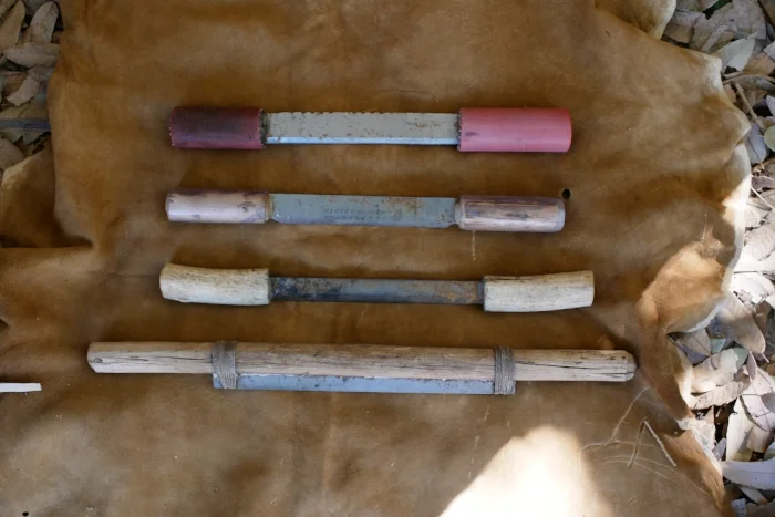 Tools made from planer blades. The top three are made from narrow blades and pretty short. The top two have handles made of wood covered with rubber or vinyl tubing. the third is antler handled and the fourth is a short blade tied into a slotted wooden handle, giving a longer working edge on a short blade.