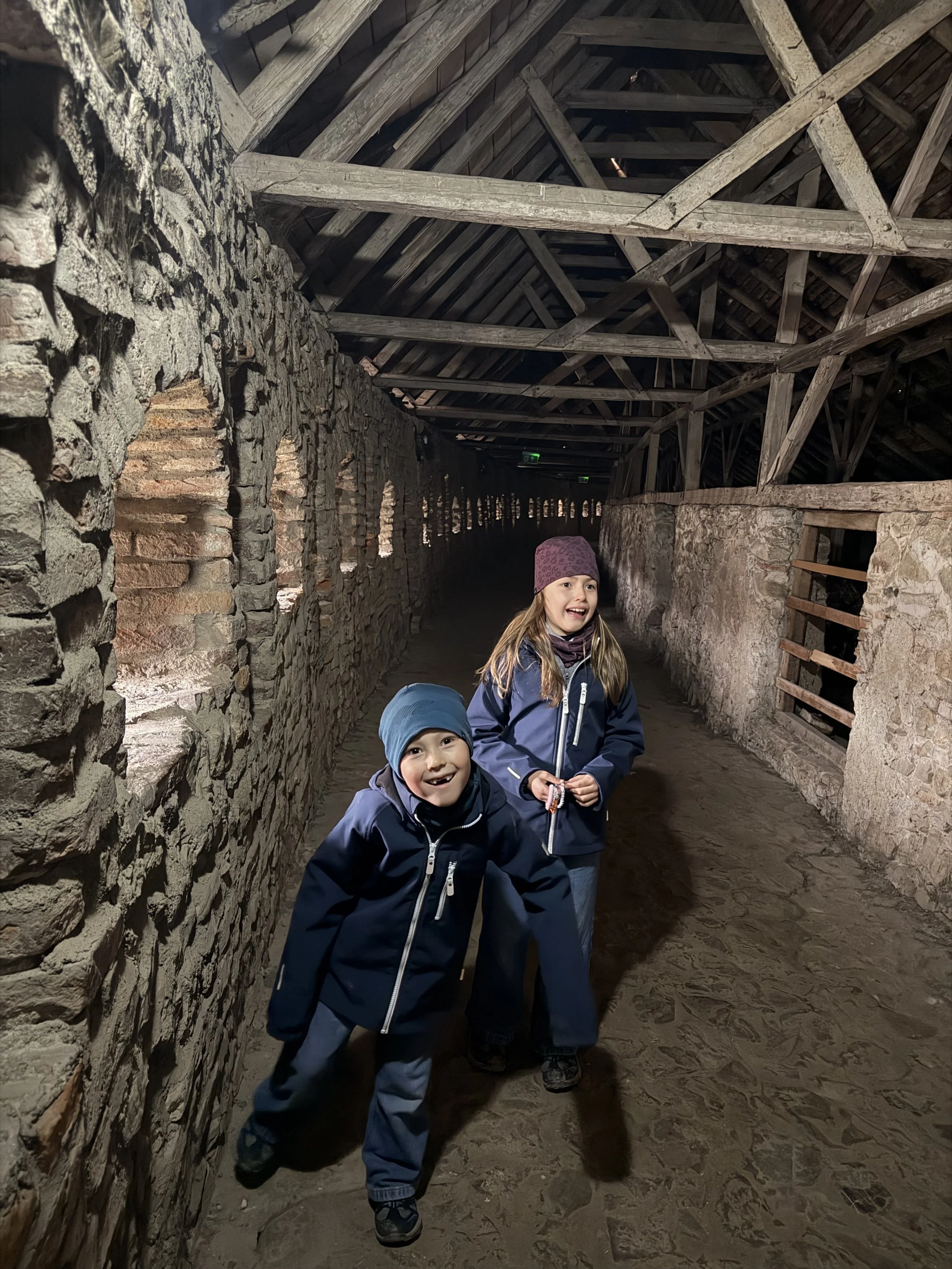Two kids exploring a stone fortress corridor at Prejmer
