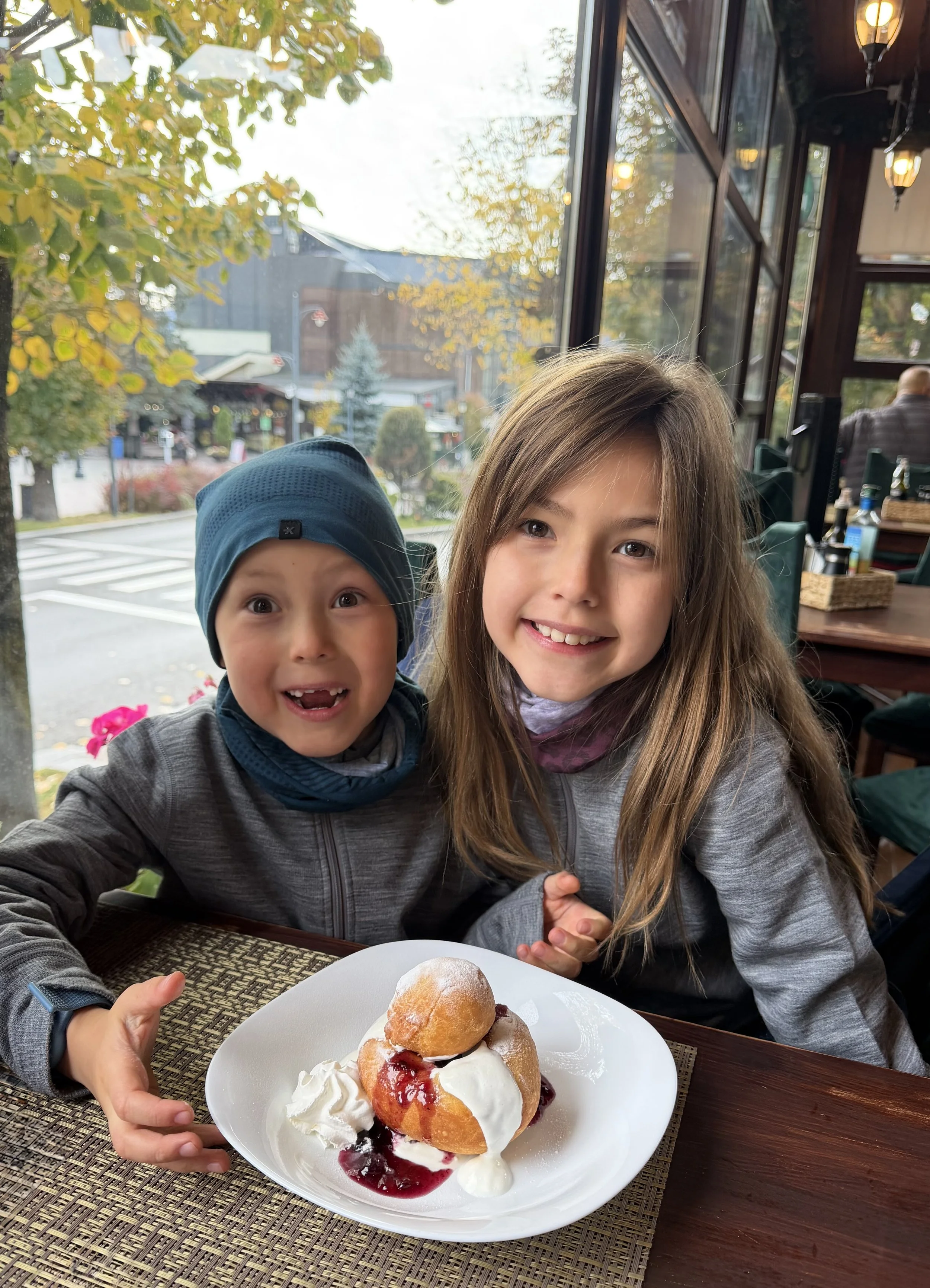 Two kids smiling over a jam-and-cream doughnut at a restaurant in Sinaia.