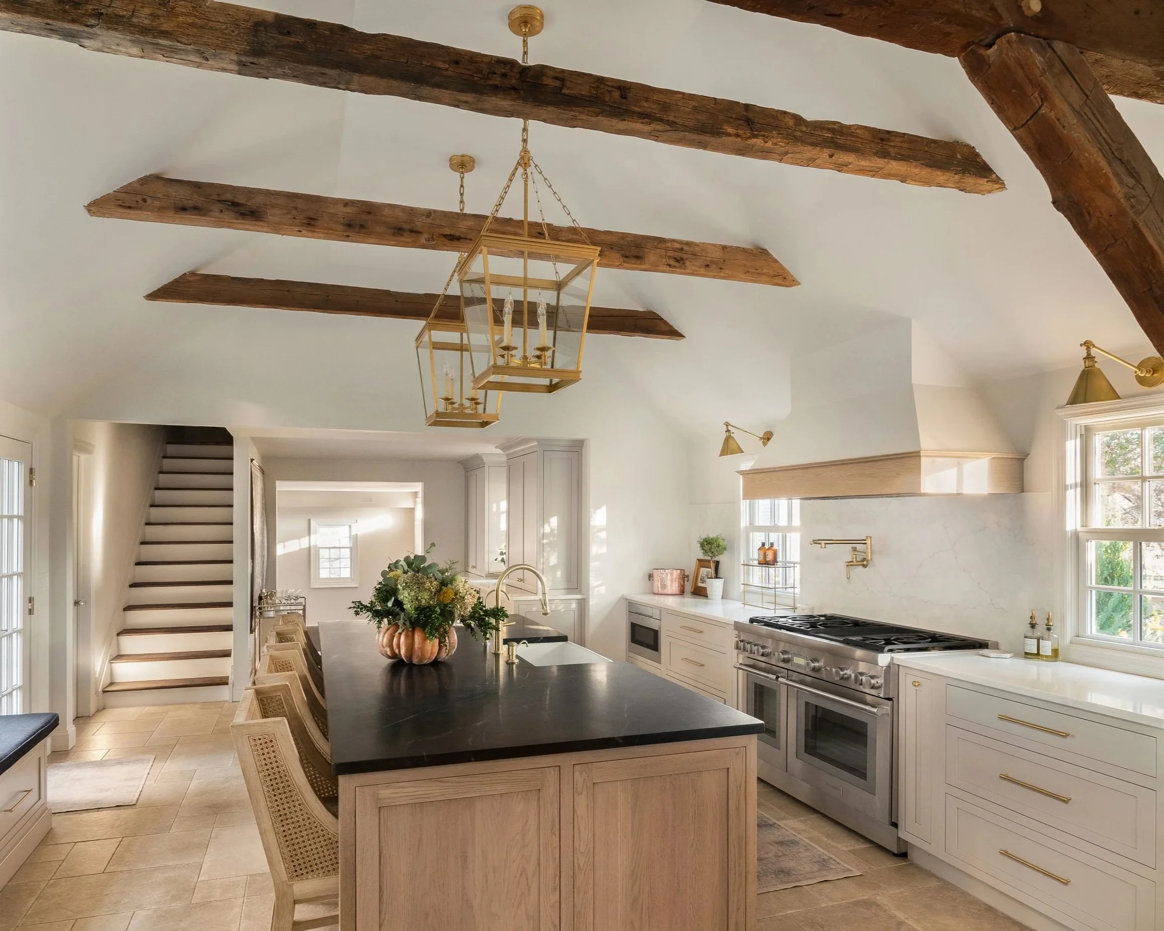 Modern kitchen with white cabinets, black countertop island, stainless steel stove, and exposed wooden ceiling beams.