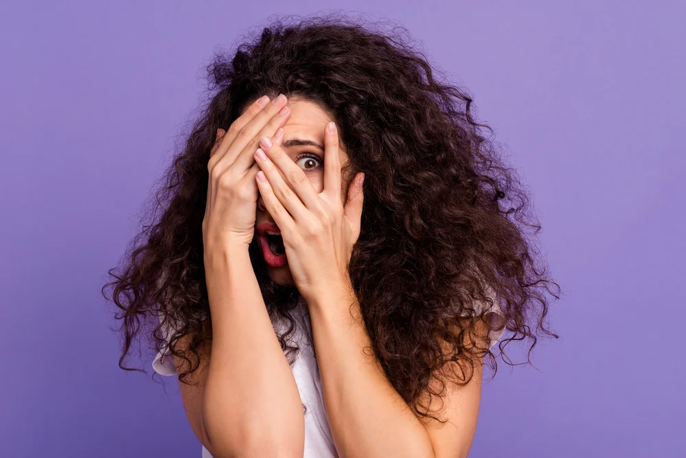 Close up photo beautiful her she lady model unexpected arms hands fingers hide face eyes full fear open mouth oh no expression wear casual white t-shirt clothes isolated violet purple background