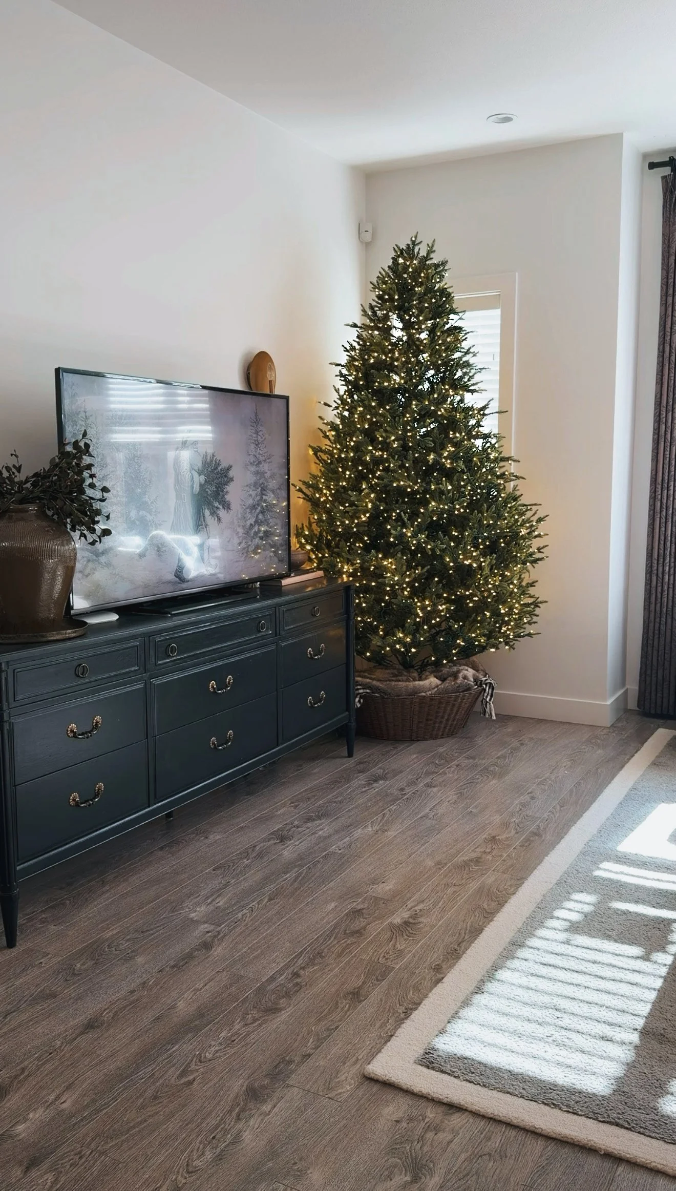 Upside-down woven tree collar filled with cream throw blankets under a lit Christmas tree