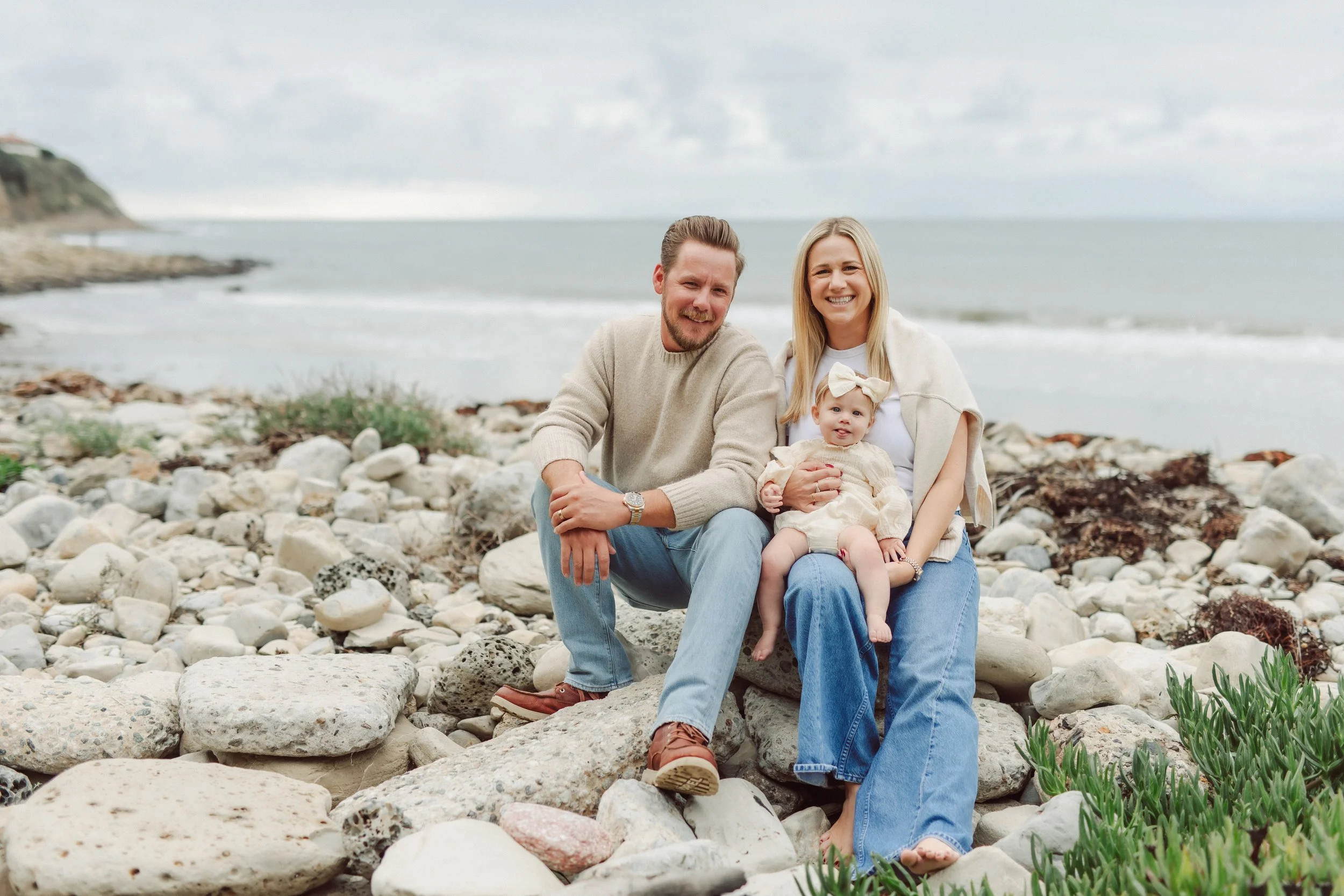 young parents with baby sit on rocky beach in Palos Verdes California