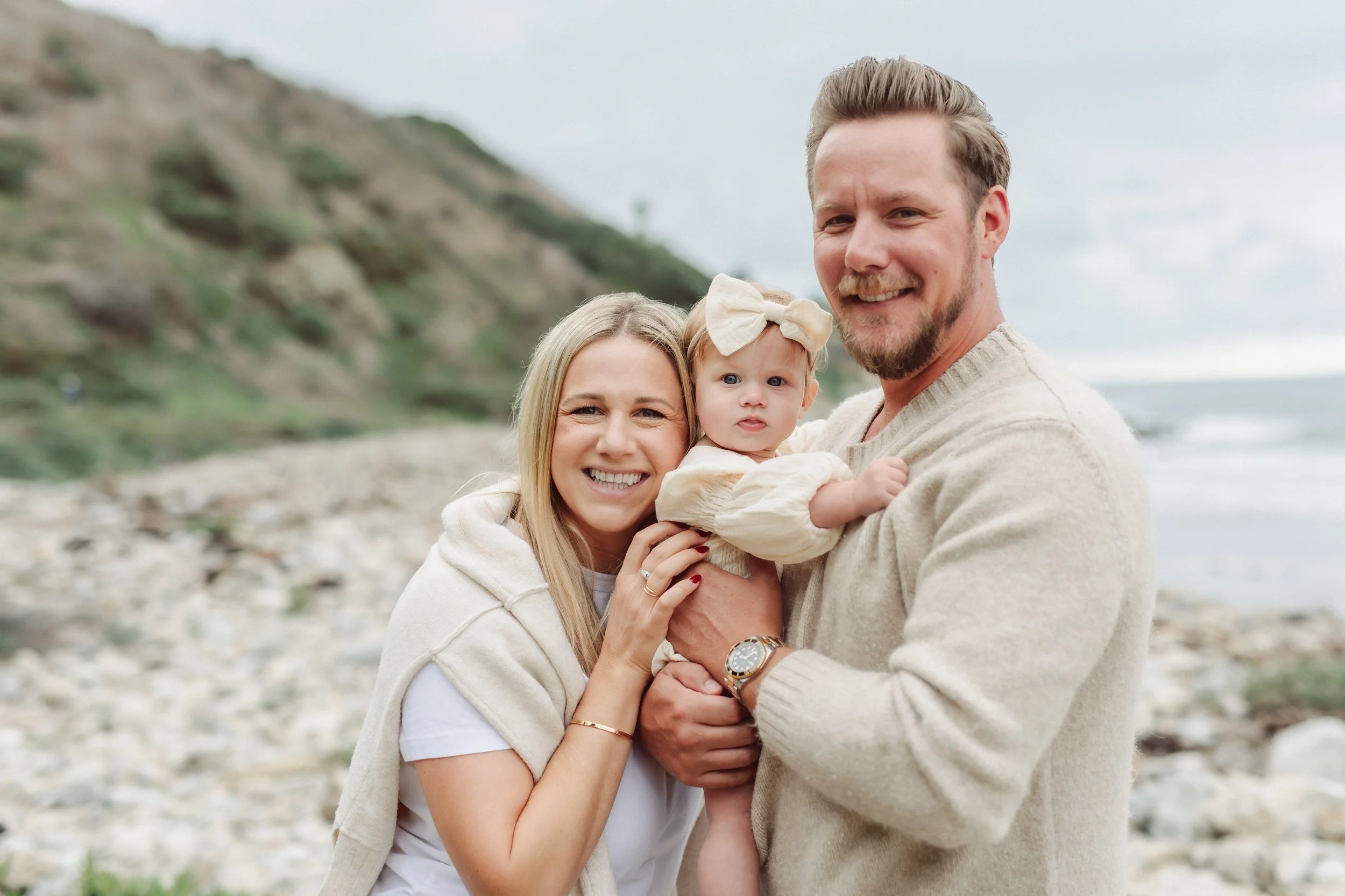 mom and dad cuddle baby on a rocky beach in california
