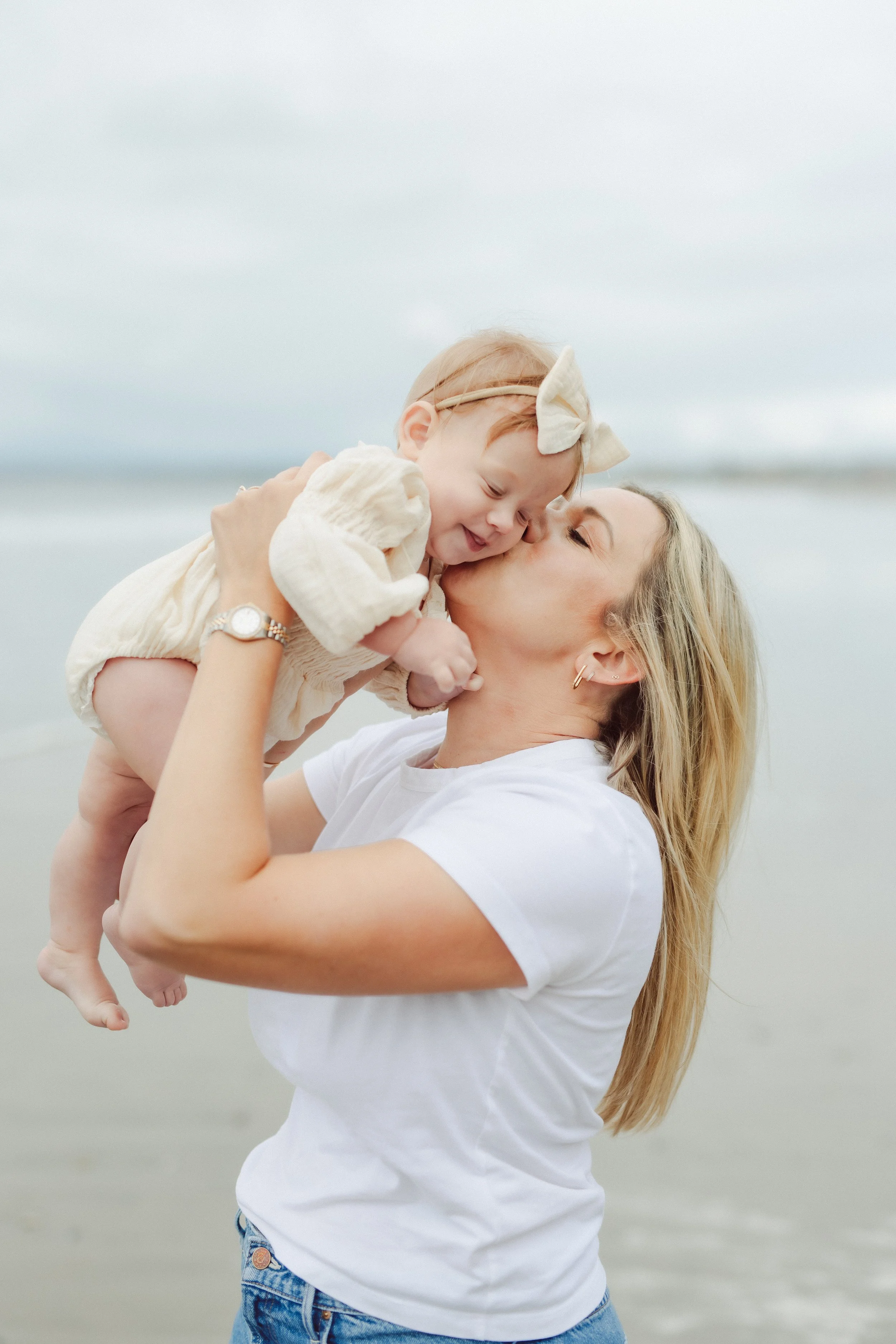 young mother kisses baby girl on a beach in Southern California