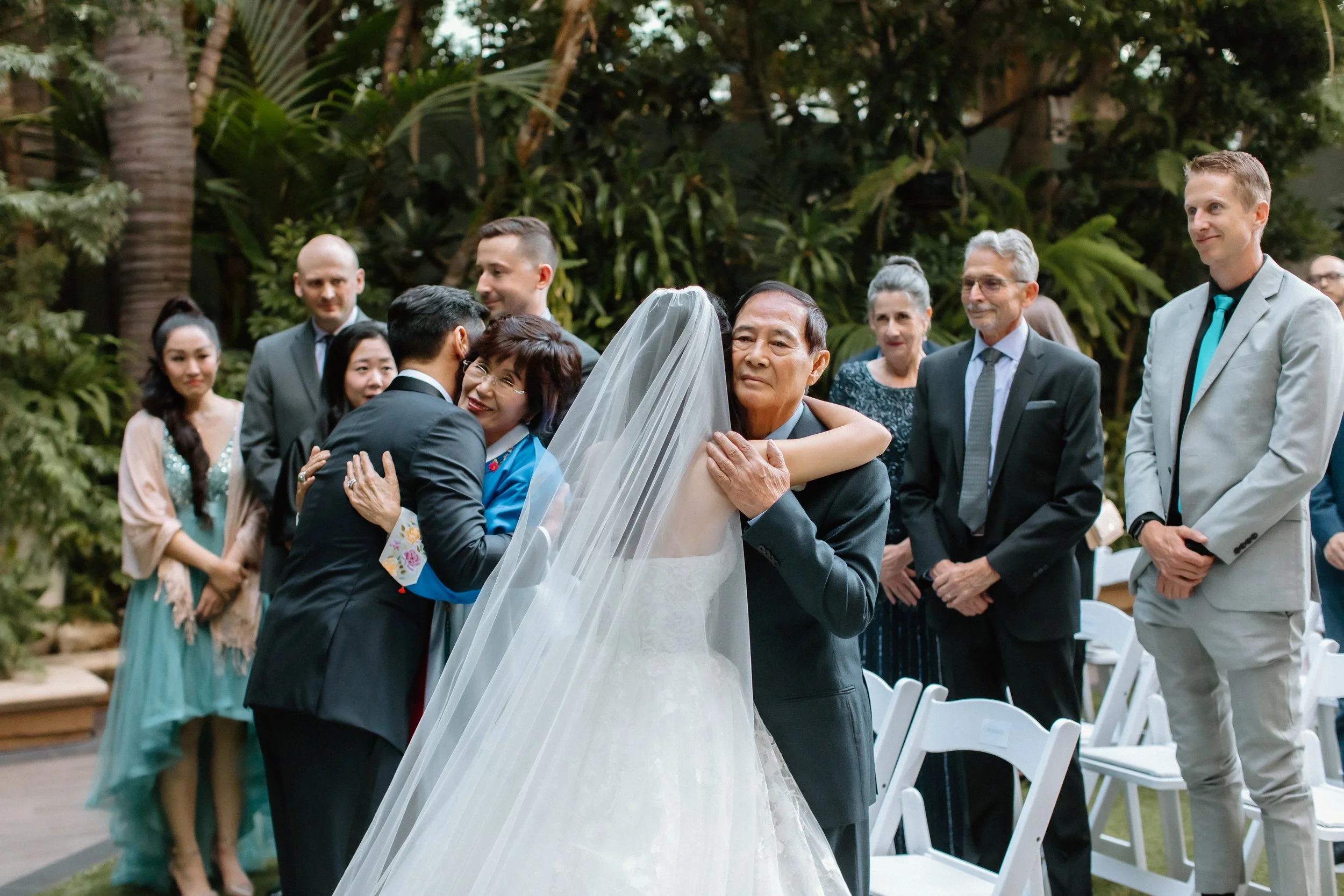 Bride and groom embrace the groom's mother and father at the beginning of the wedding ceremony