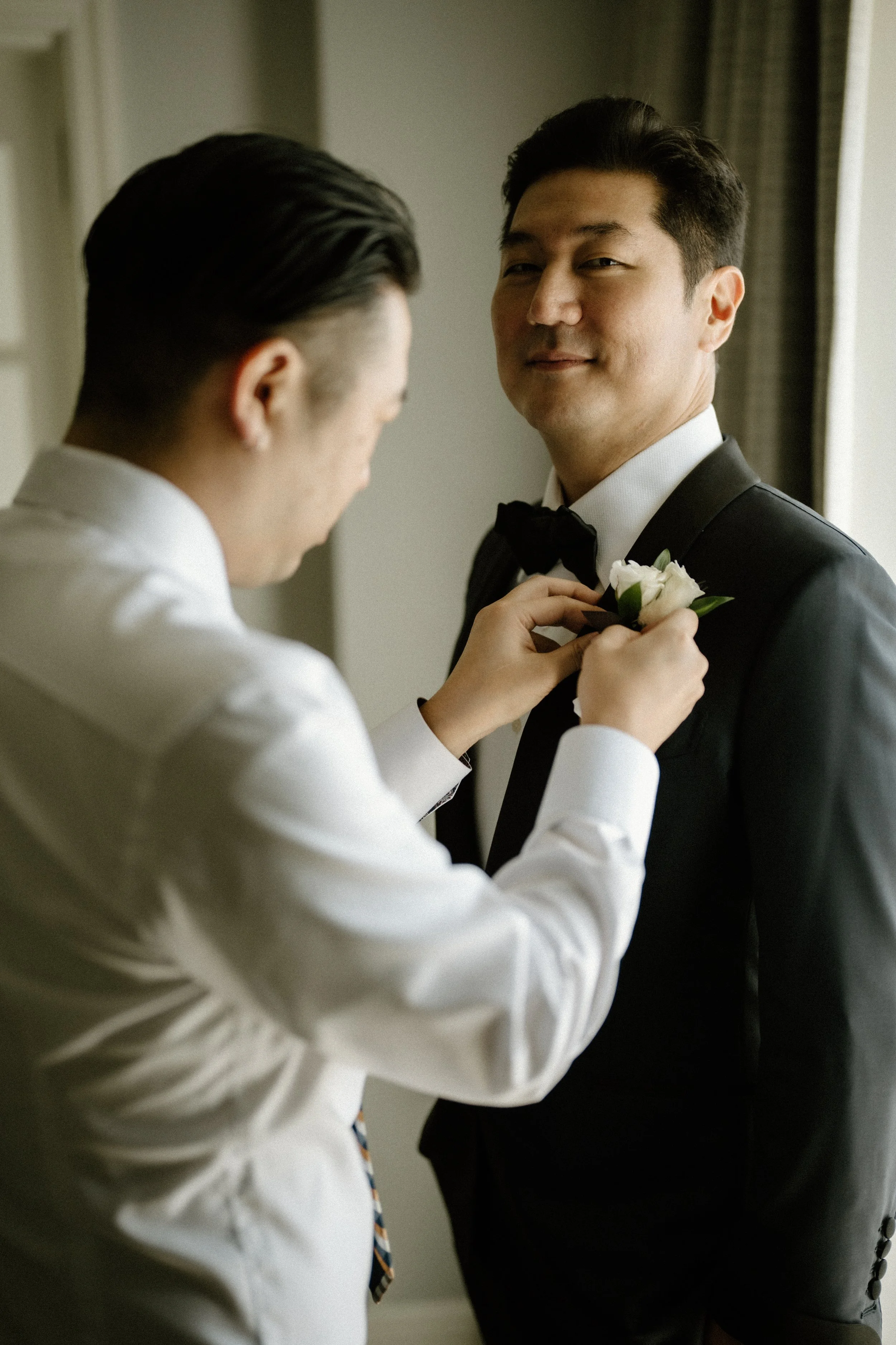 Groomsman helps secure white ranunculus boutonniere to Groom's Tuxedo Jacket. 