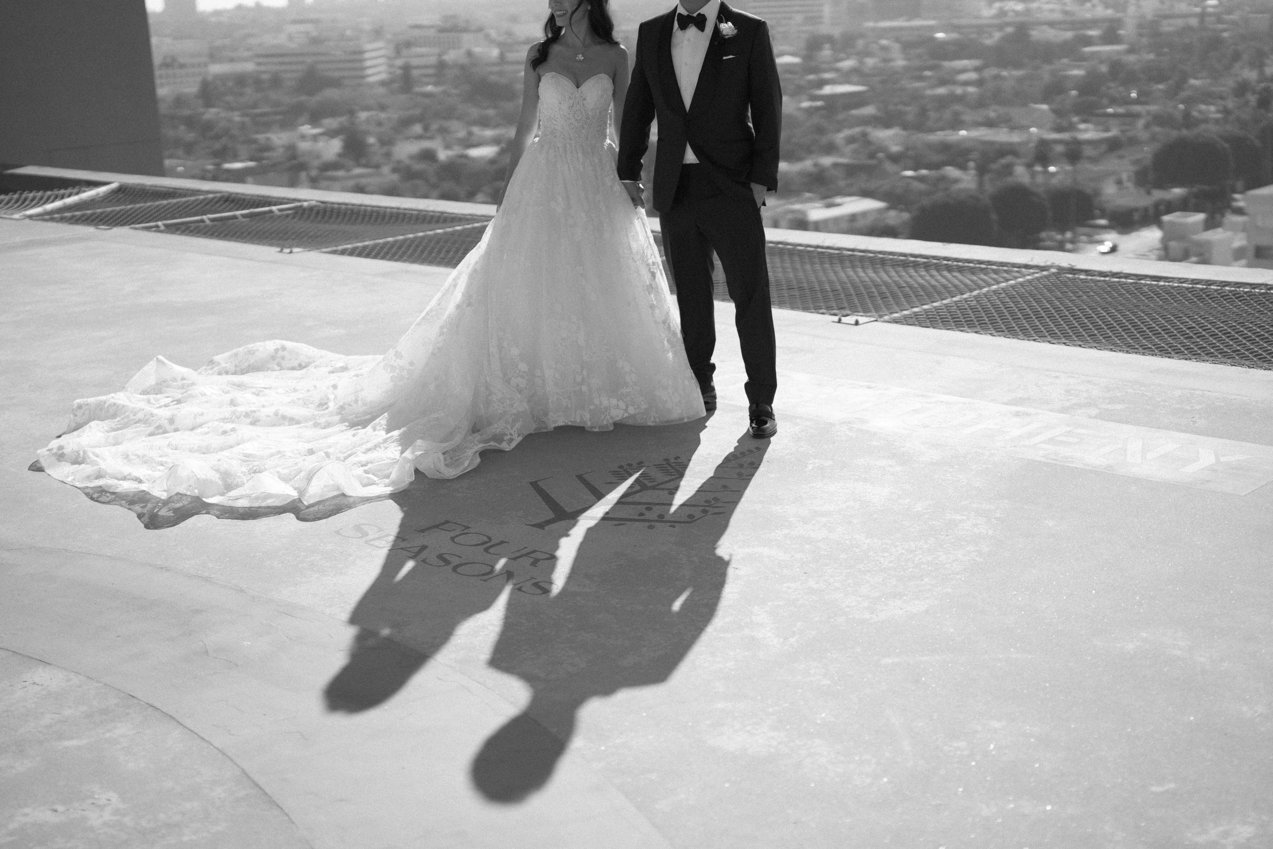 Black and white photograph of Bride in pronovias ballgown and groom standing with shadow outlining Four Seasons Hotel logo with the city of los angeles in the background