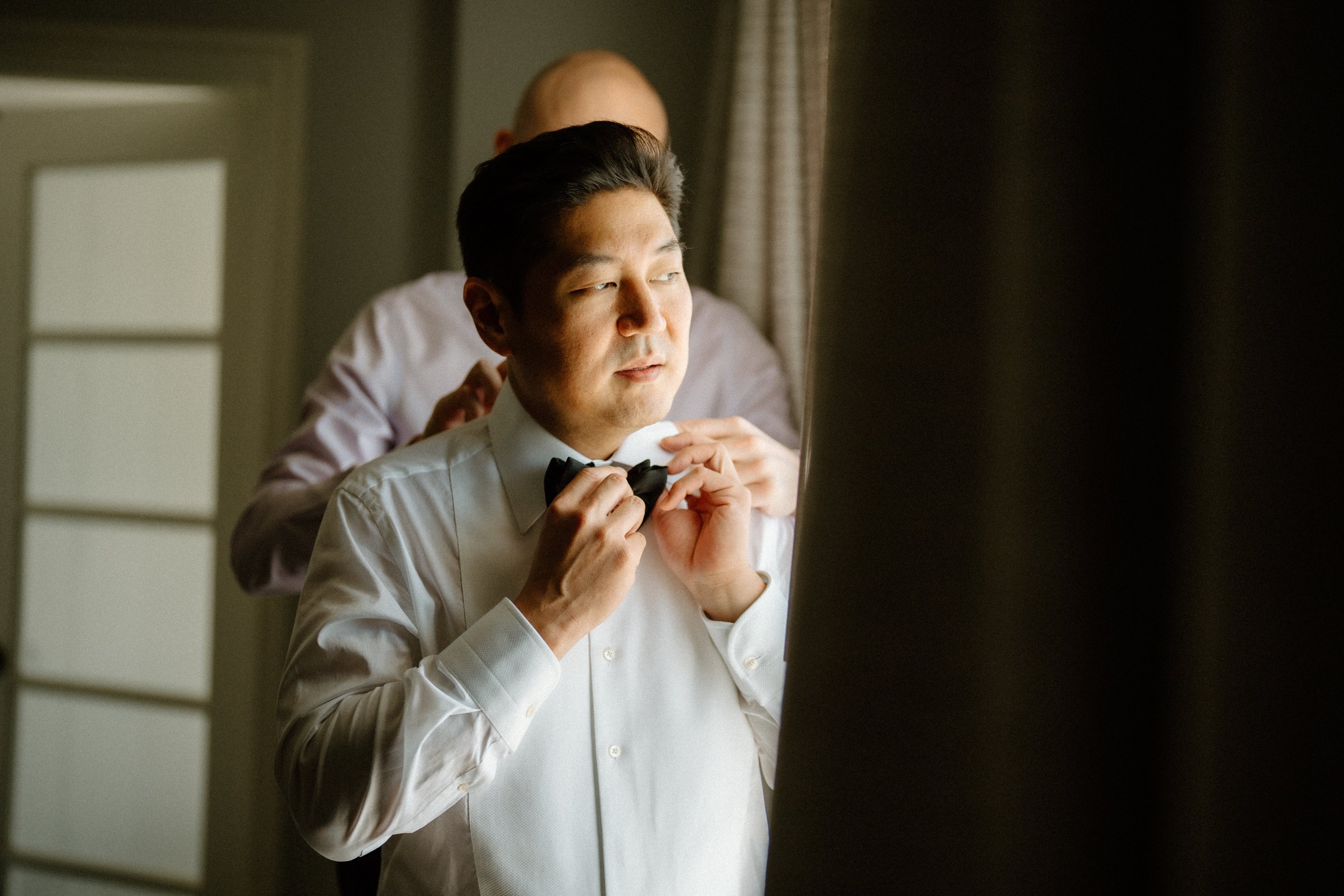 Best Man assists groom with bow tie in his suite at Four Seasons Hotel