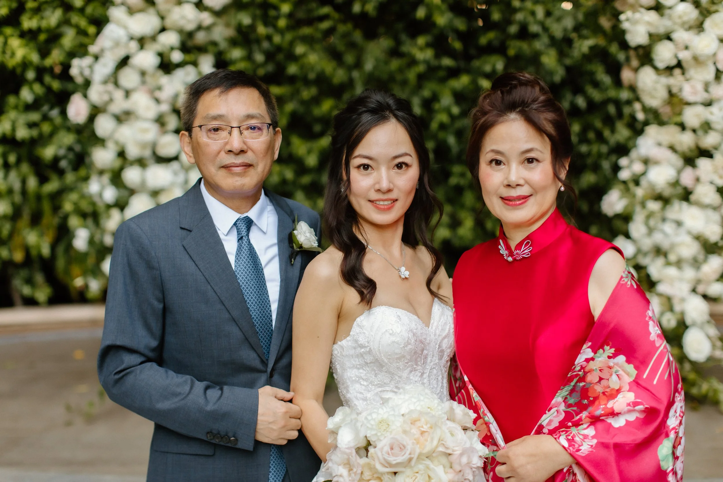 Bride in Pronovias gown with her parents in front of flower arch at Four Seasons Hotel