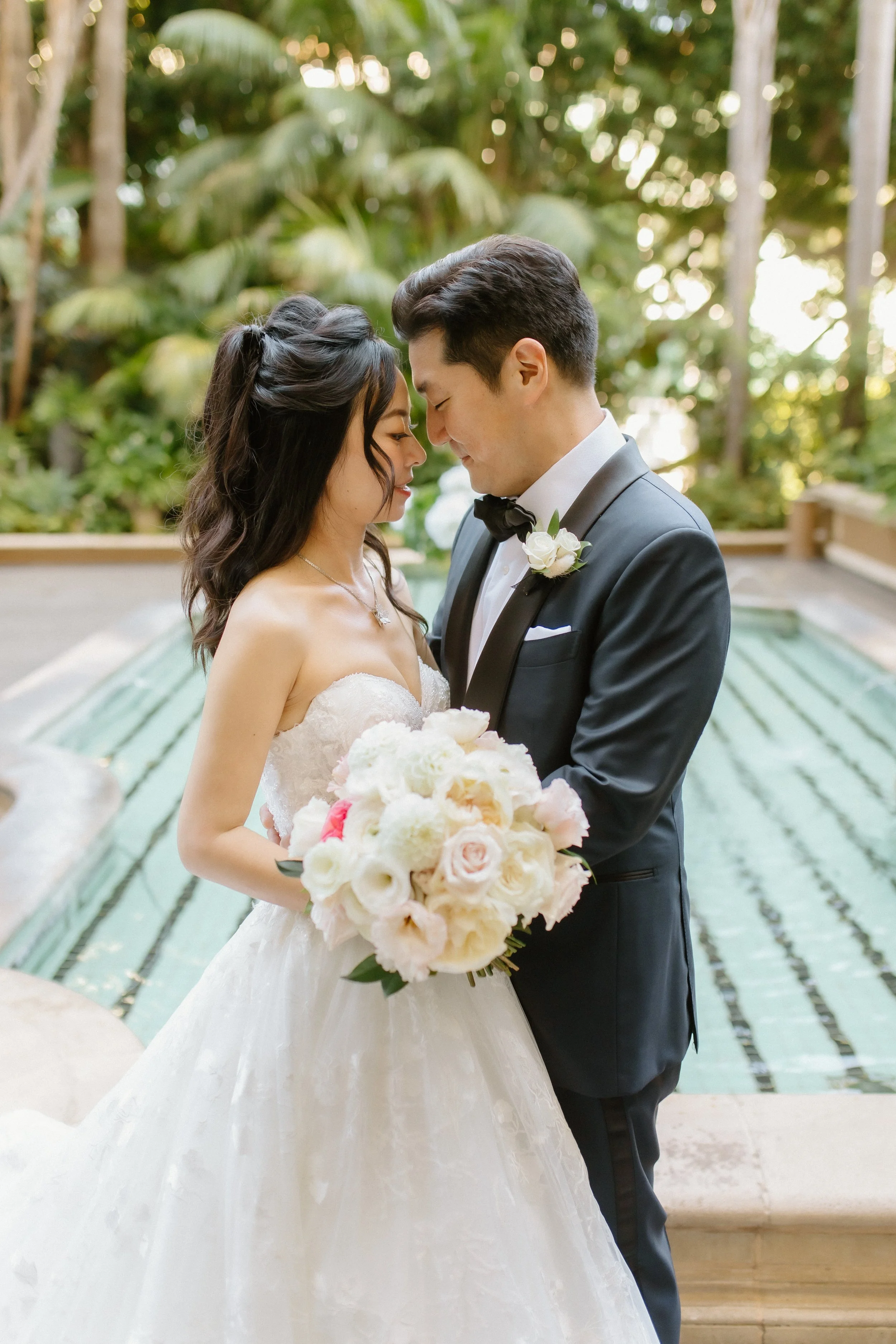 Bride in Pronovias ballgown and Groom in Navy and black tuxedo embrace in front of the fountain in the garden of Four Season Hotel Los Angeles at Beverly Hills