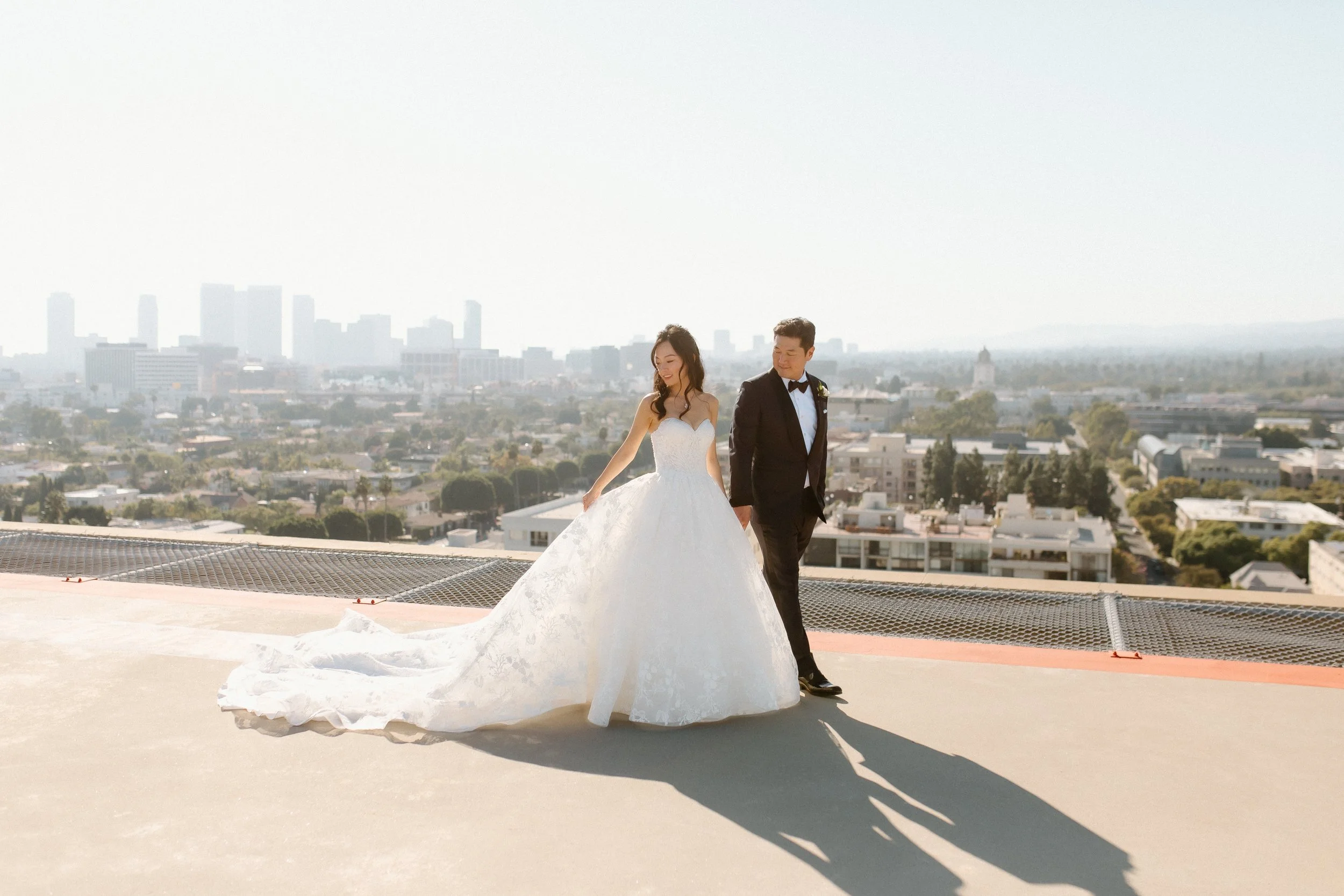 Bride in Pronovias ballgown and Groom stroll across Helipad on Four Seasons Hotel Los Angeles at Beverly Hills with Los Angeles Skyline in the distance