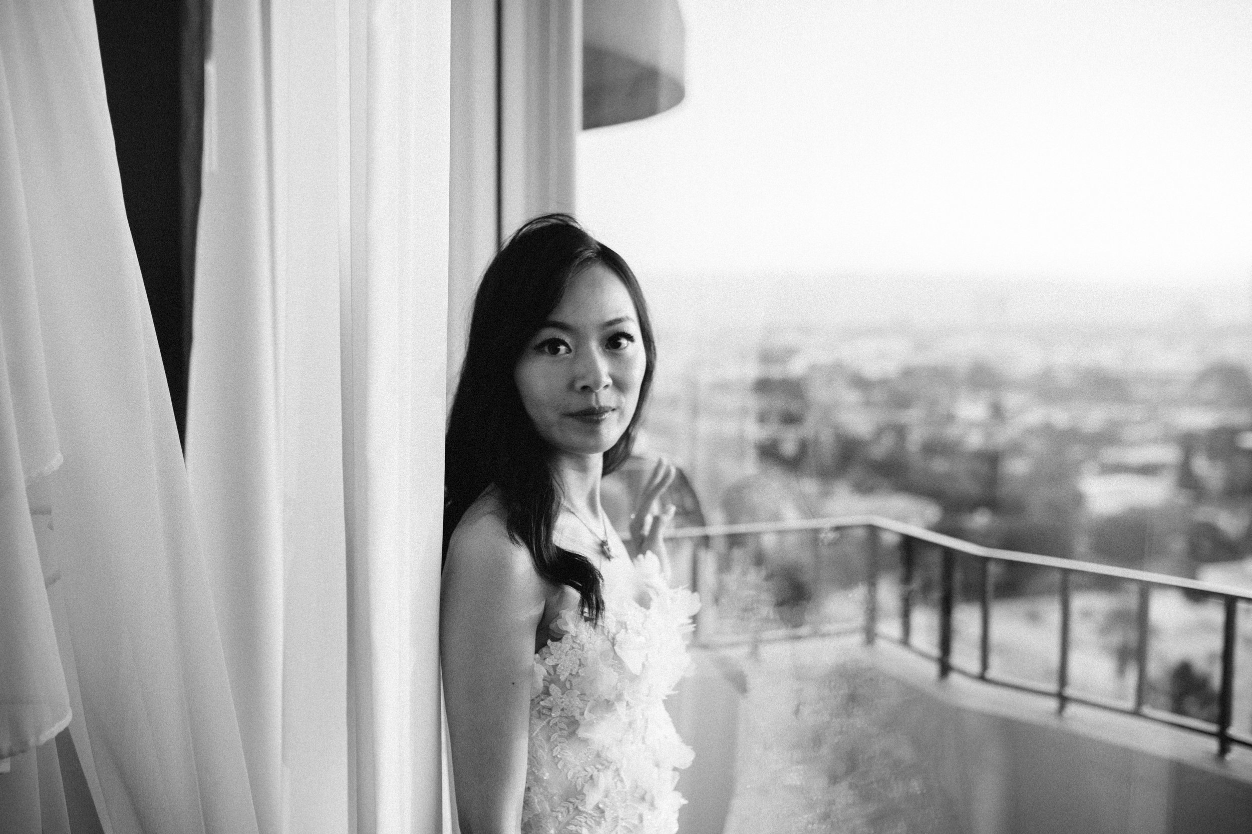 Bride stands by window of her balcony in her reception gown by Pronovias.