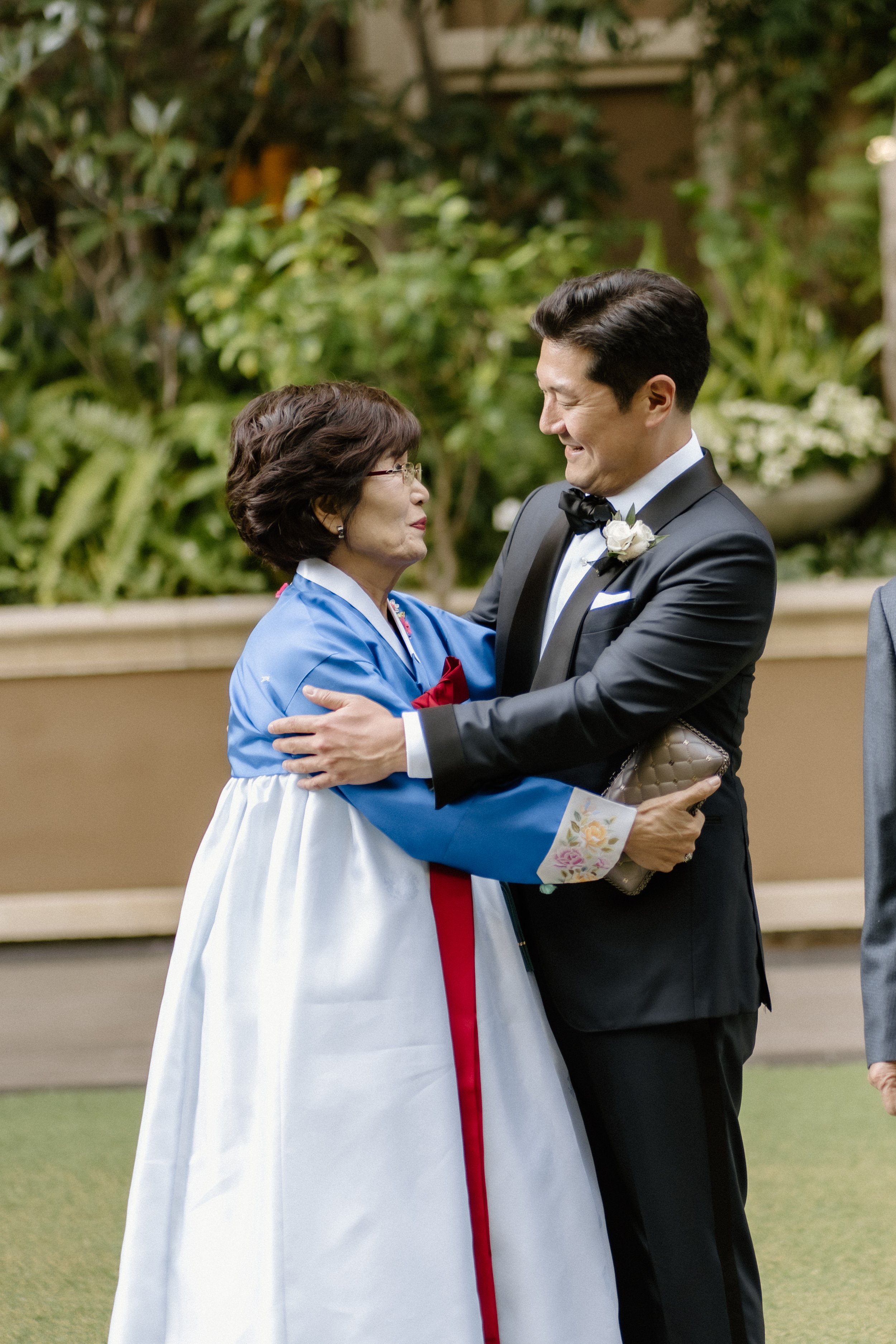 Groom greeting his mother who is wearing a traditional Korean Hanbok in the garden at Four Seasons Hotel before the wedding ceremony