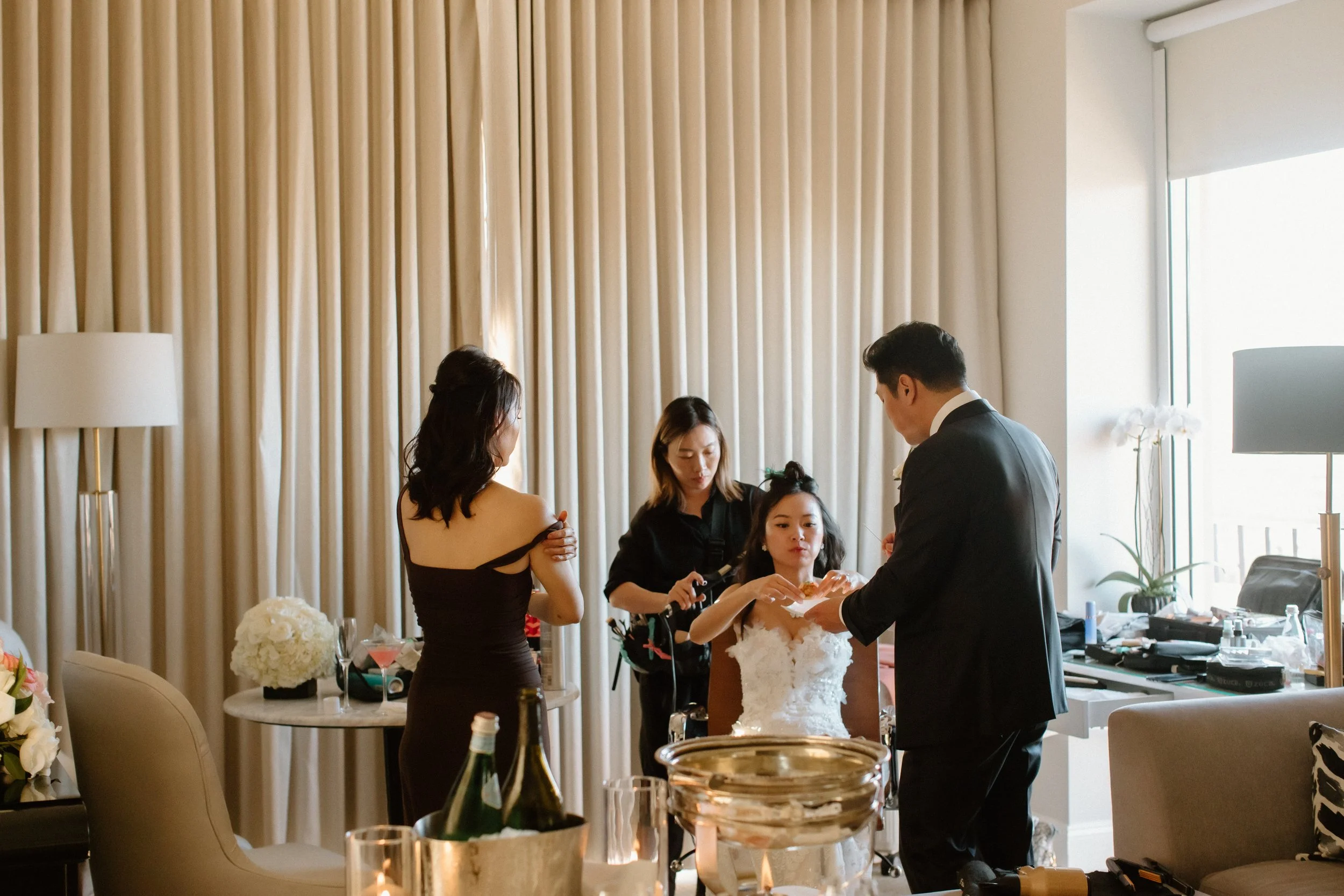 Groom feeds the bride hors d'oeuvres as she has her hair redone by Kelly Zhang Agency after the ceremony in anticipation of the reception at Four Seasons Hotel