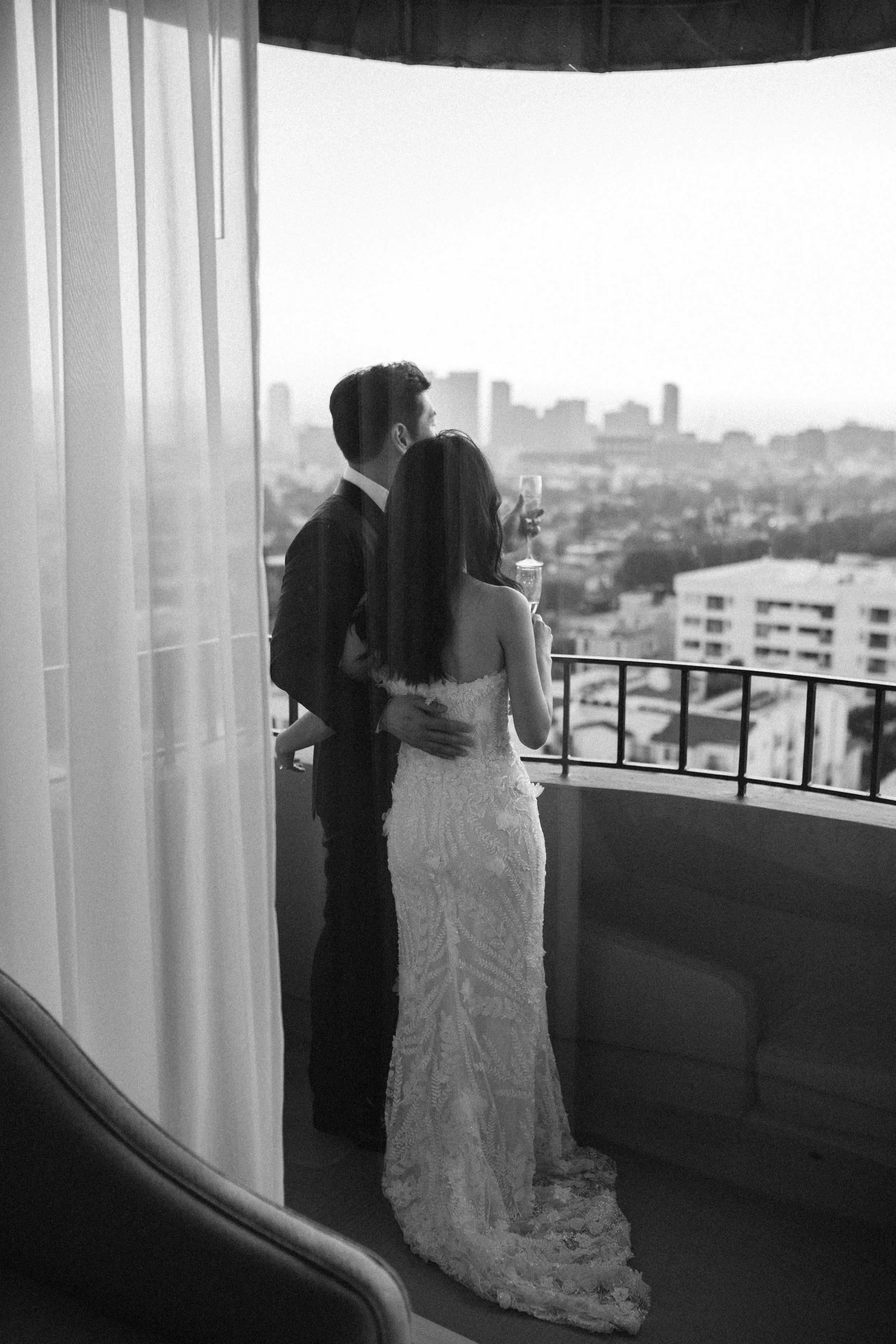 Black and white photograph of a bride and groom standing on the balcony of the wedding suite at Four Seasons Hotel Los Angeles as they share a quiet moment of reflection.