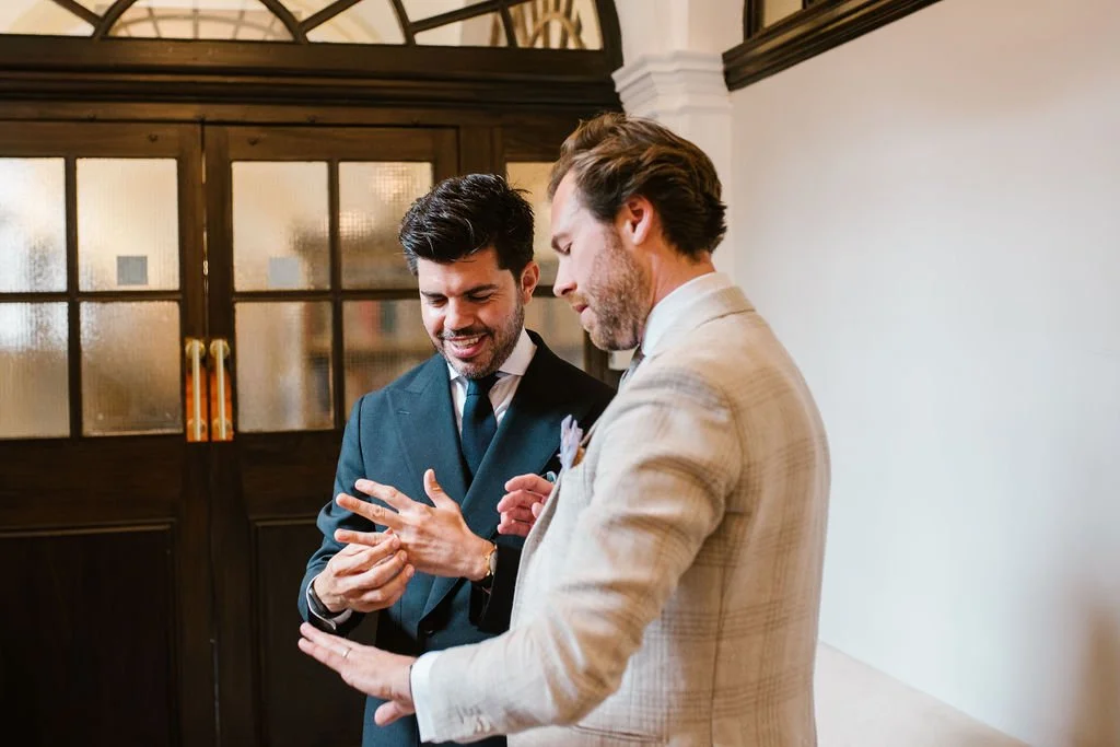 Two men in formal attire smiling and having a conversation indoors.