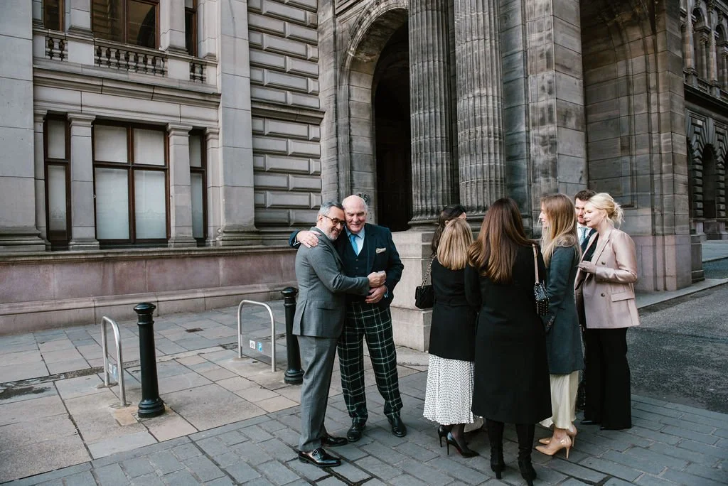 Group of people chatting on a city sidewalk in front of a historical building with large columns.