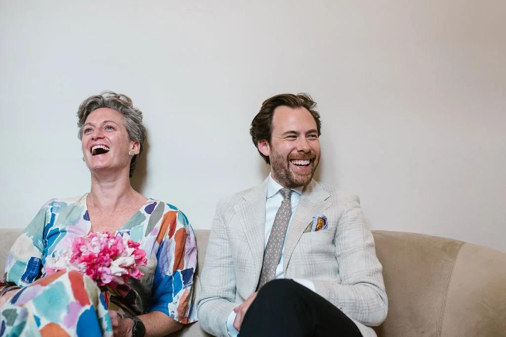 A woman and a man sitting on a beige couch, laughing.
