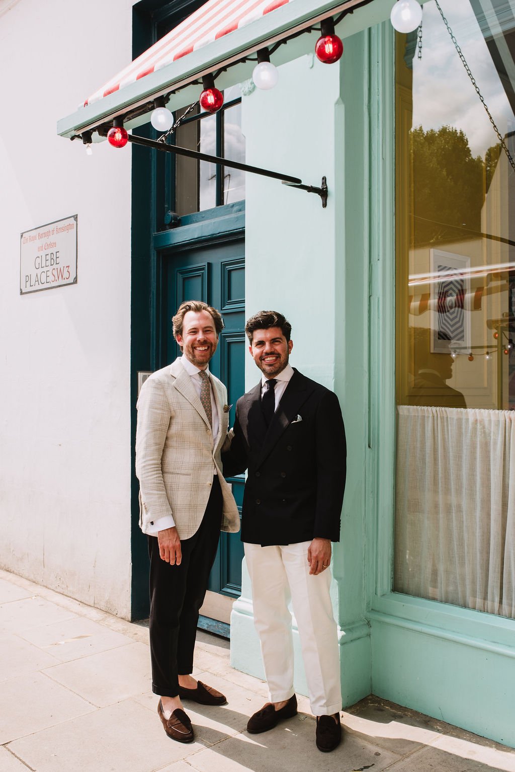 Two men in suits standing outside a colorful building, smiling at the camera.