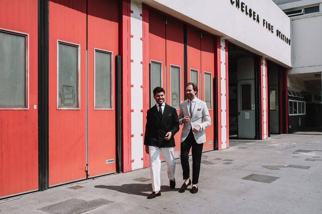 Two men in suits walking and talking outside Chelsea Fire Station.